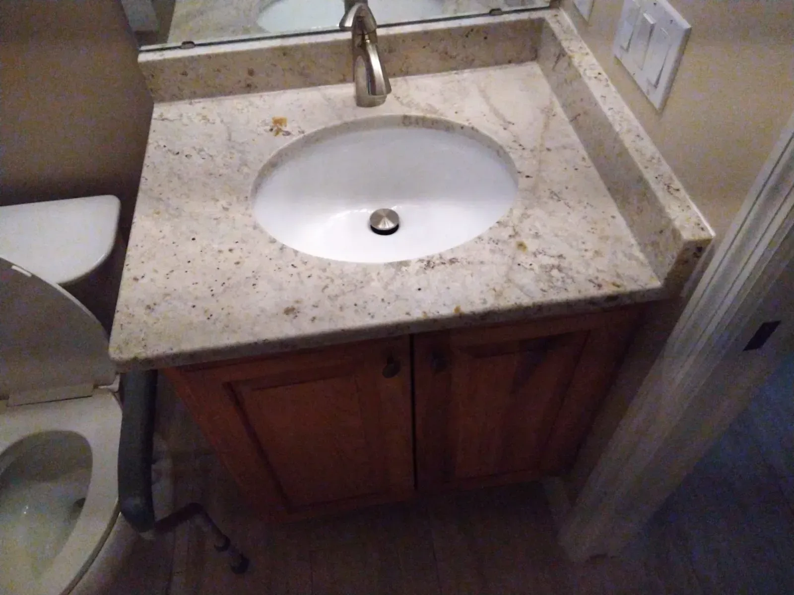 Bathroom sink with speckled countertop, white basin, and wooden cabinet below.