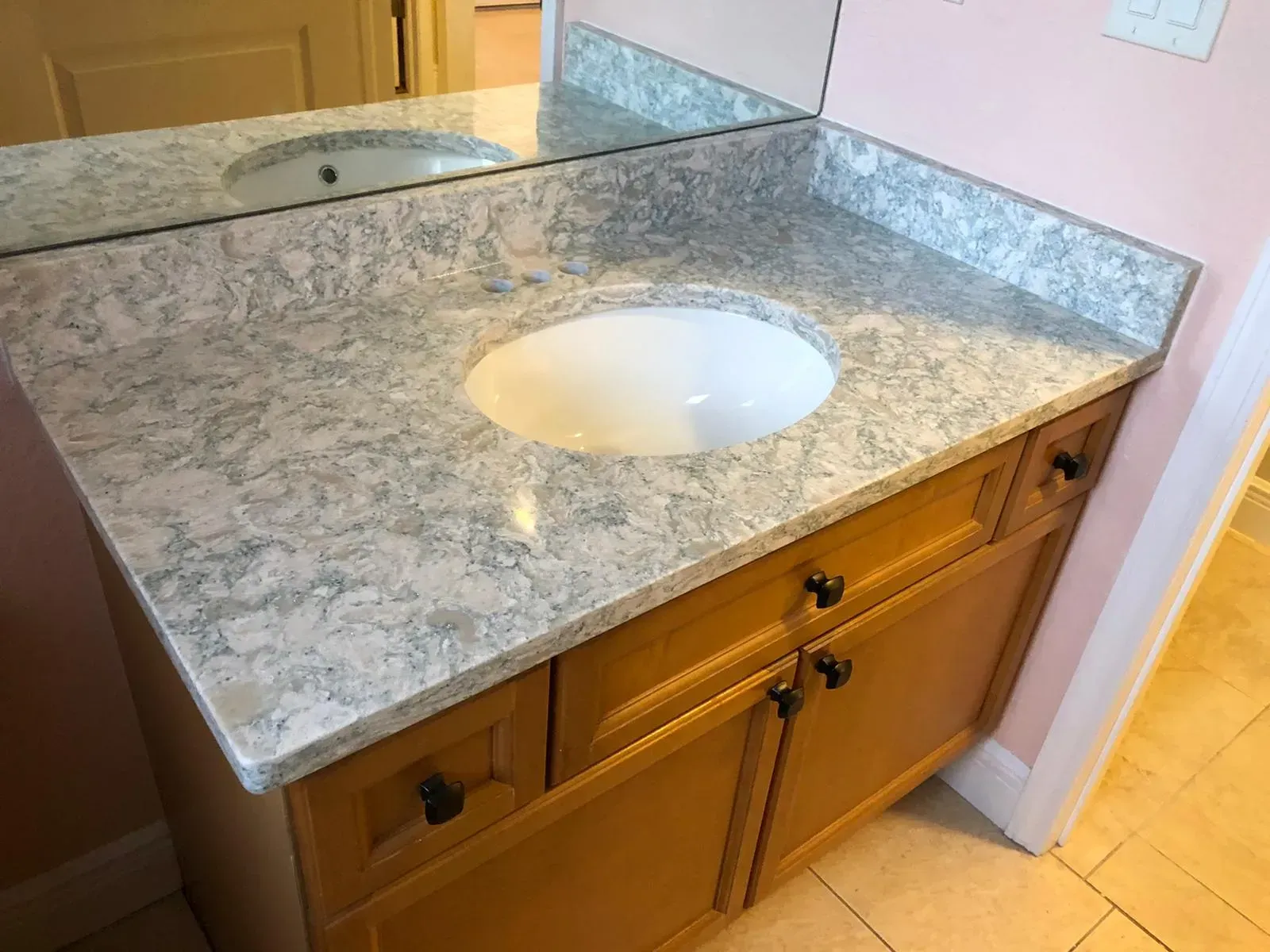 Bathroom vanity with gray granite countertop, white sink, and light wood cabinets￼