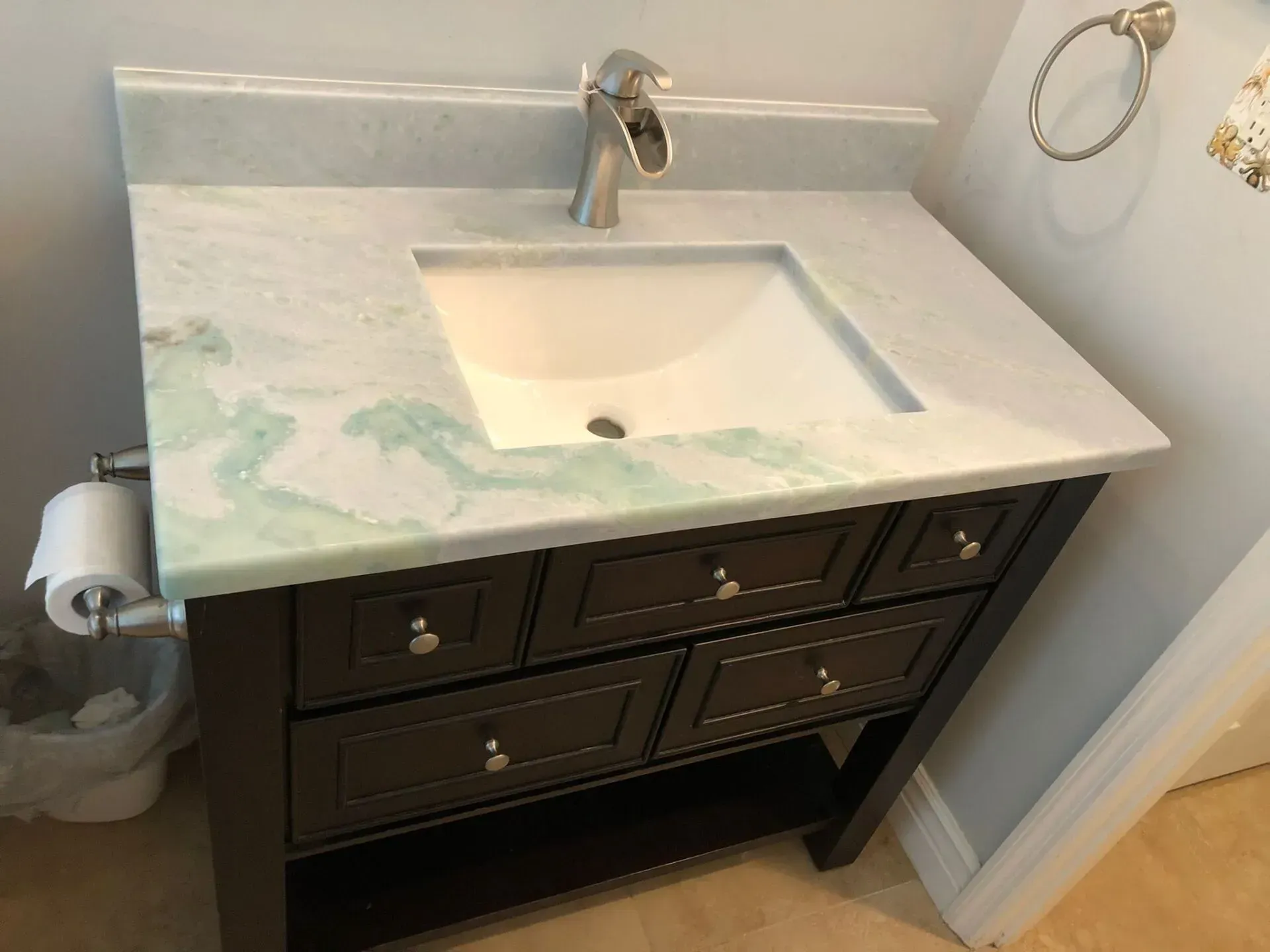 Bathroom vanity with white sink, dark cabinet, and marble countertop against a light wall.