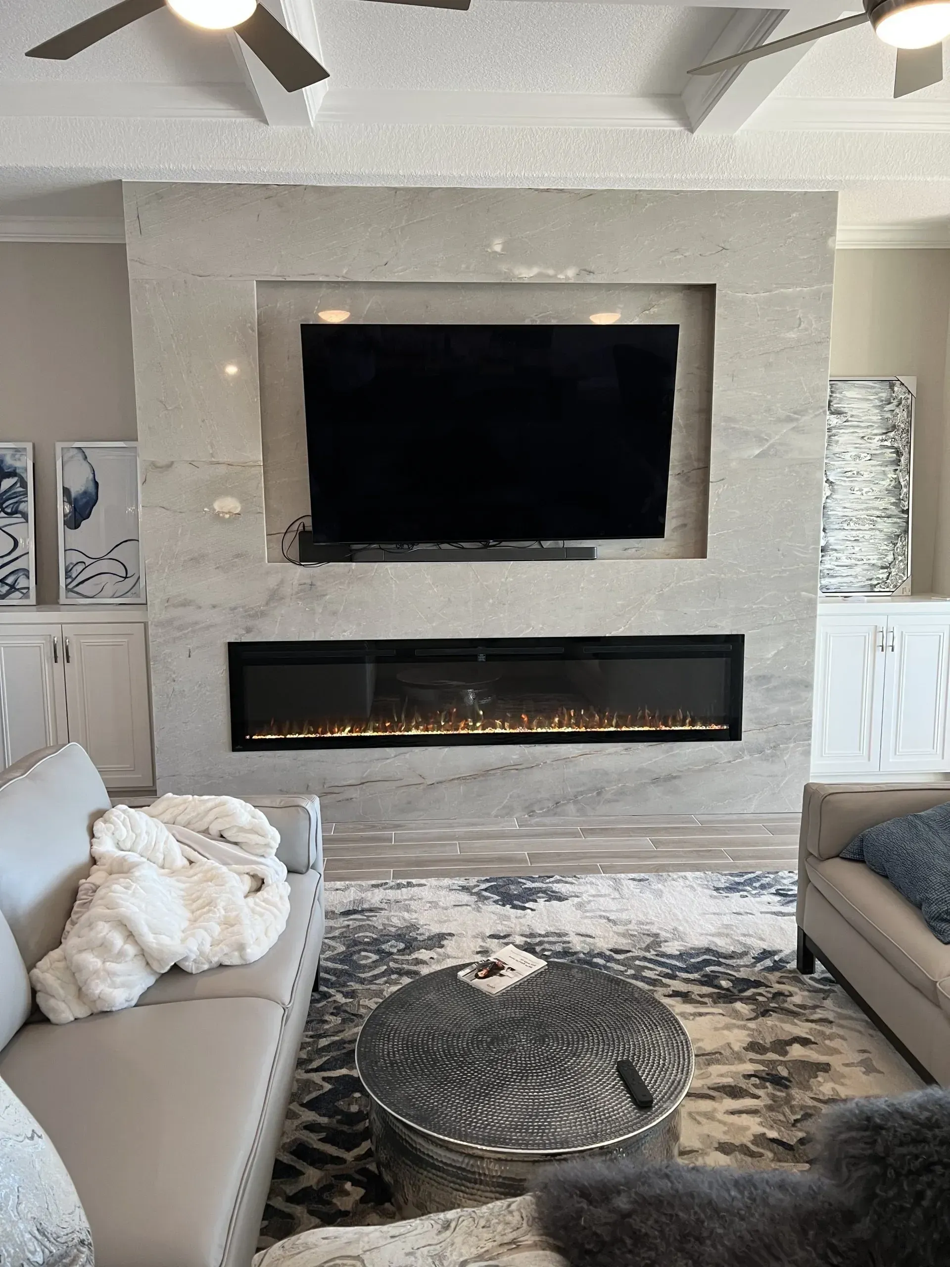 Modern living room with stone fireplace, mounted TV, lit linear fire, and neutral seating area