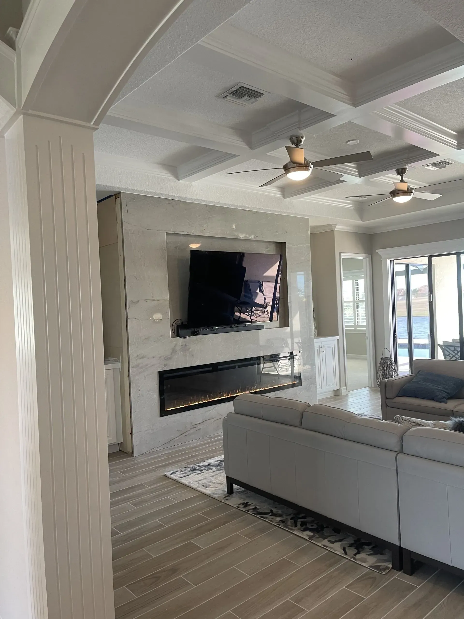 Modern living room with gray sectional, wall-mounted TV, fireplace, and ceiling fans