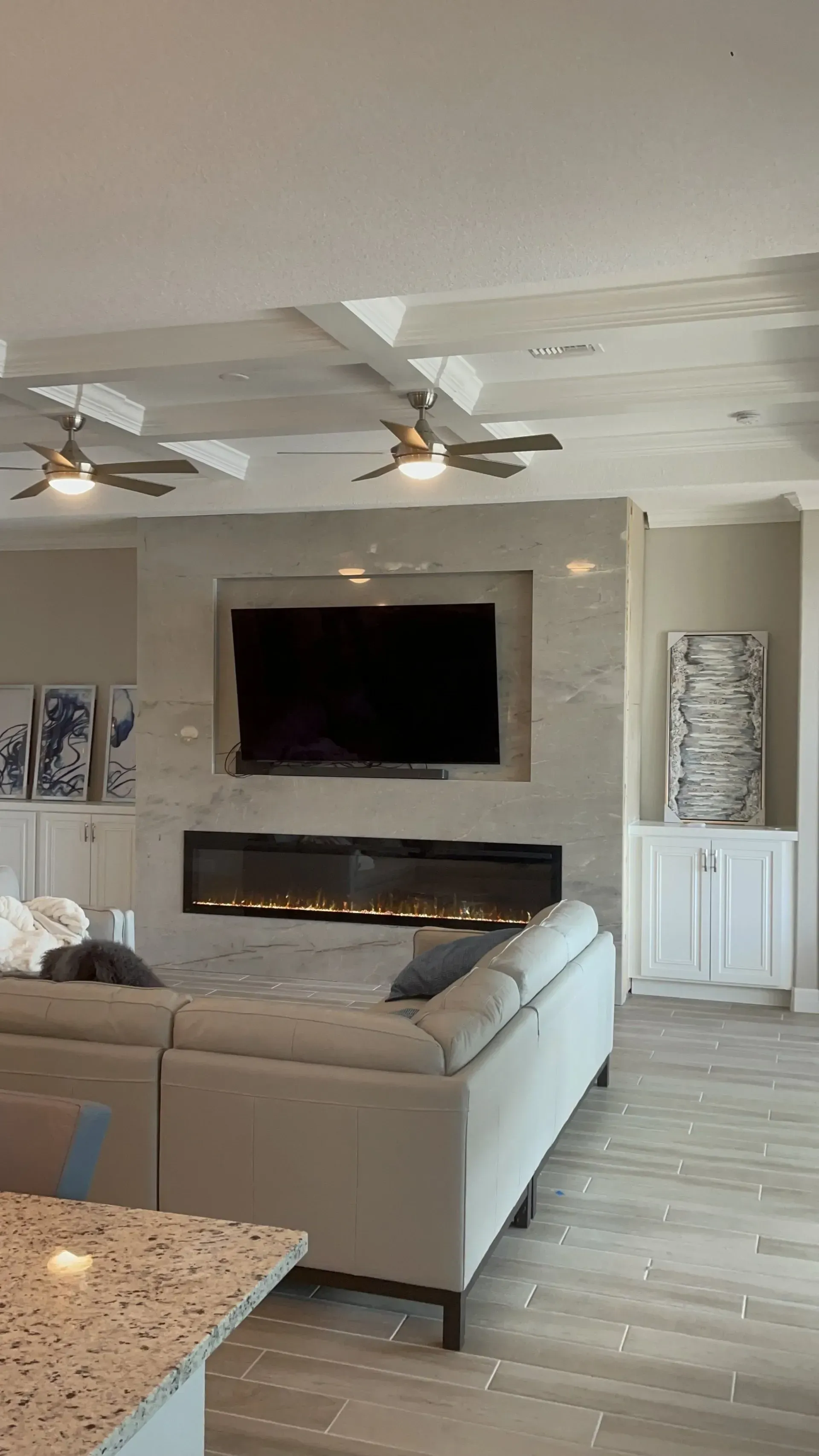 Modern living room with sectional sofa, wall-mounted TV over fireplace, and ceiling fans under a white ceiling.