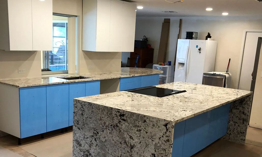 Modern kitchen with blue cabinets, granite island, and white refrigerator under recessed lights