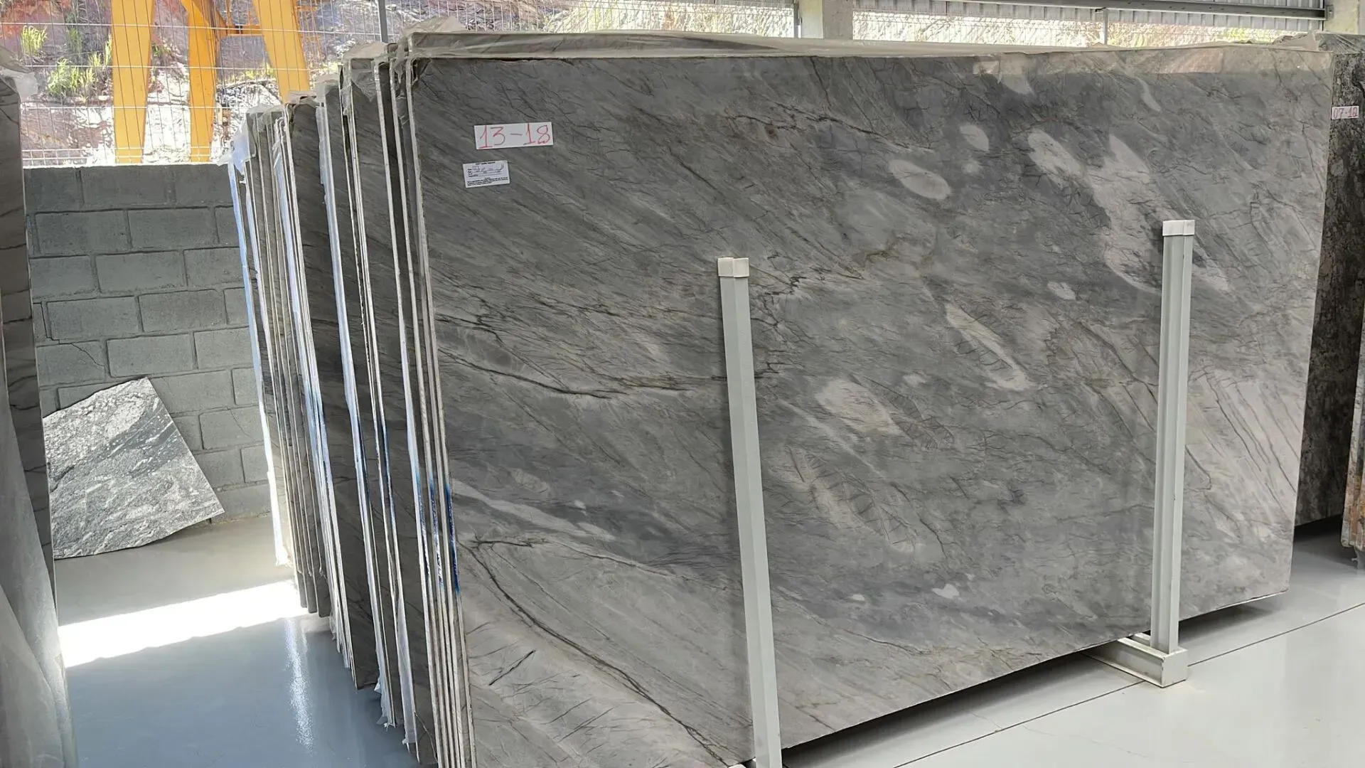 Large gray marble slab standing on white support rails in a warehouse or stone yard