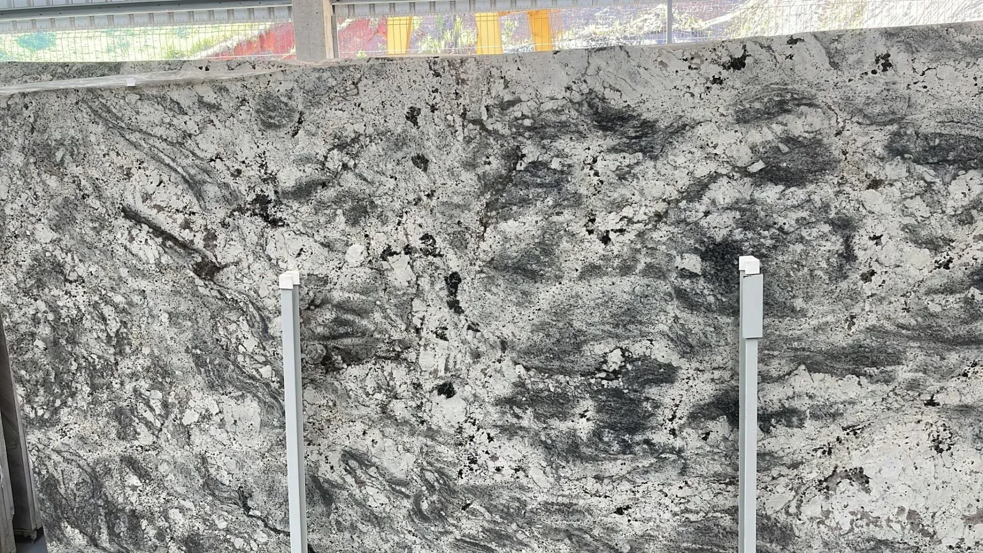 Mottled gray concrete wall with vertical metal posts in front and a strip of painted pavement above
