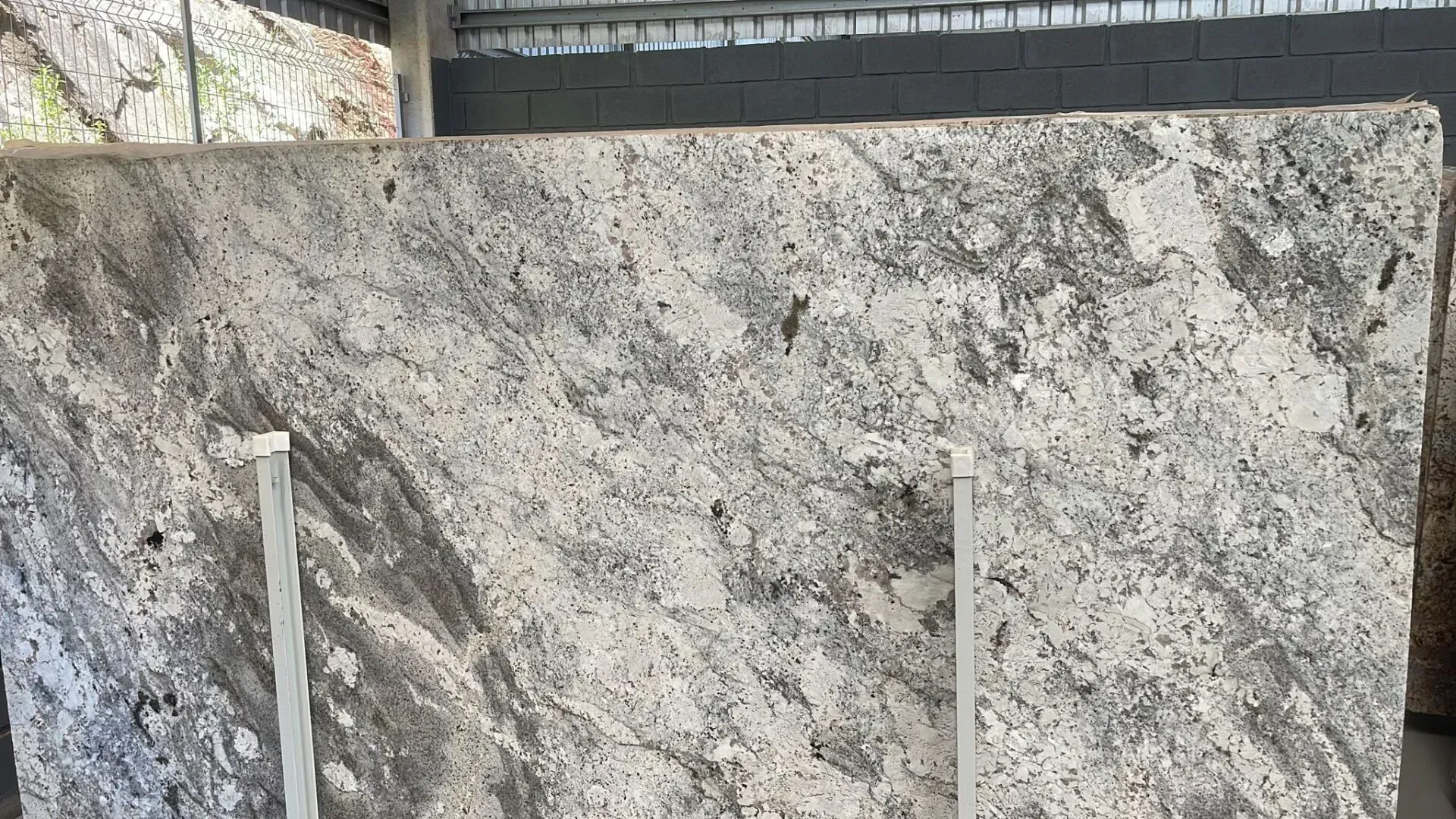 Stone wall with a rough gray surface and two white vertical pipes or rails in front