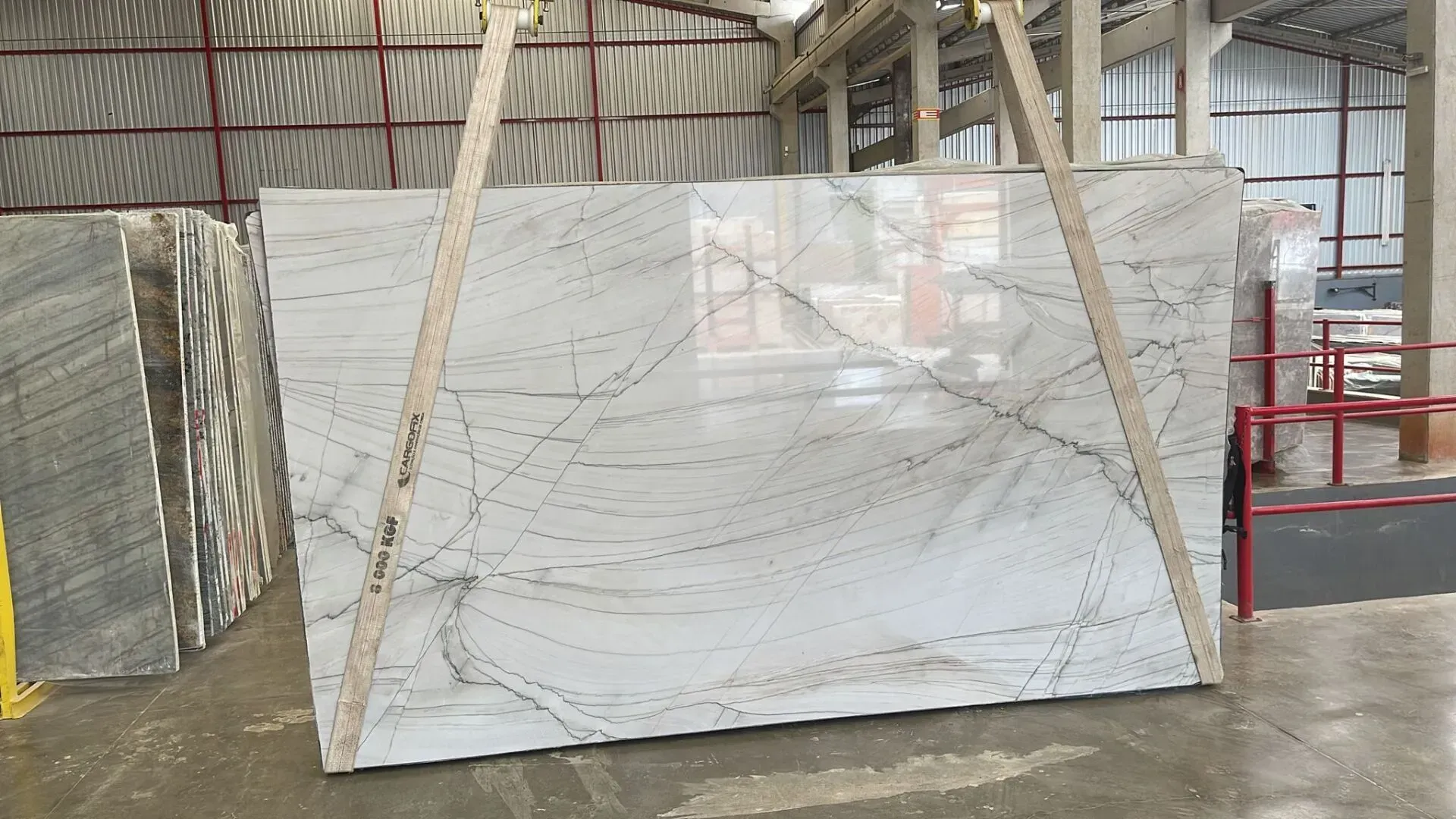 Large white marble slab wrapped in plastic, leaning on wooden supports inside a warehouse.