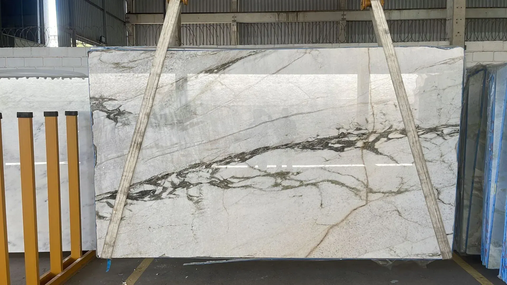 Large white marble slab with gray veining leaning on a rack in a warehouse setting