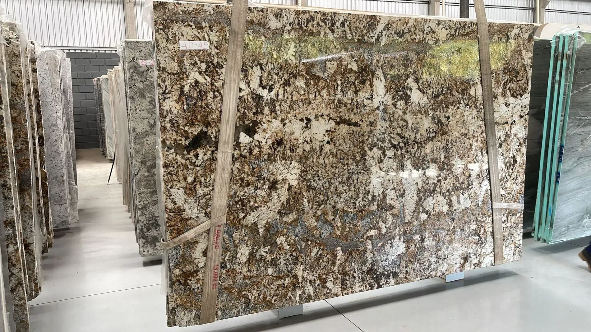 Rows of large polished stone slabs in a warehouse, with brown and white speckled surfaces.