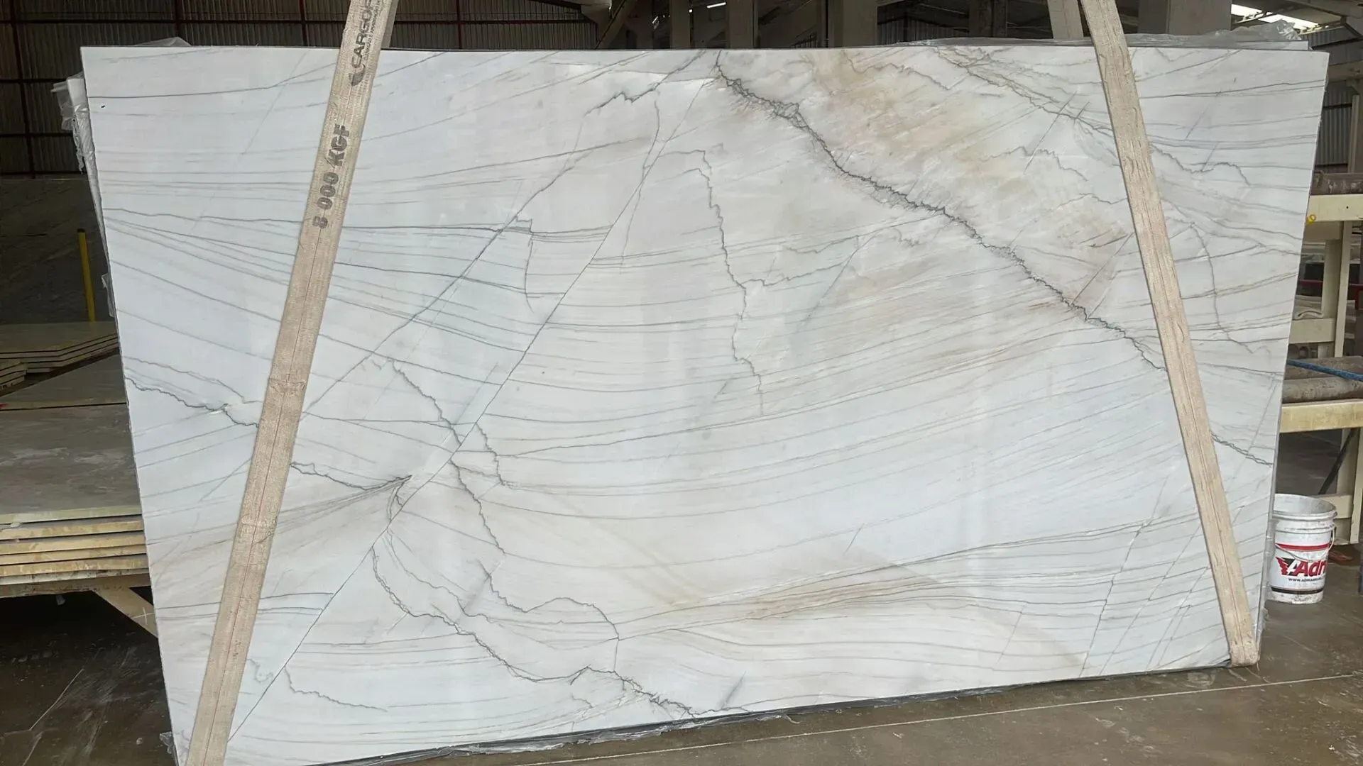 Large white marble slab with gray veining leaning on wooden supports in a warehouse-like setting
