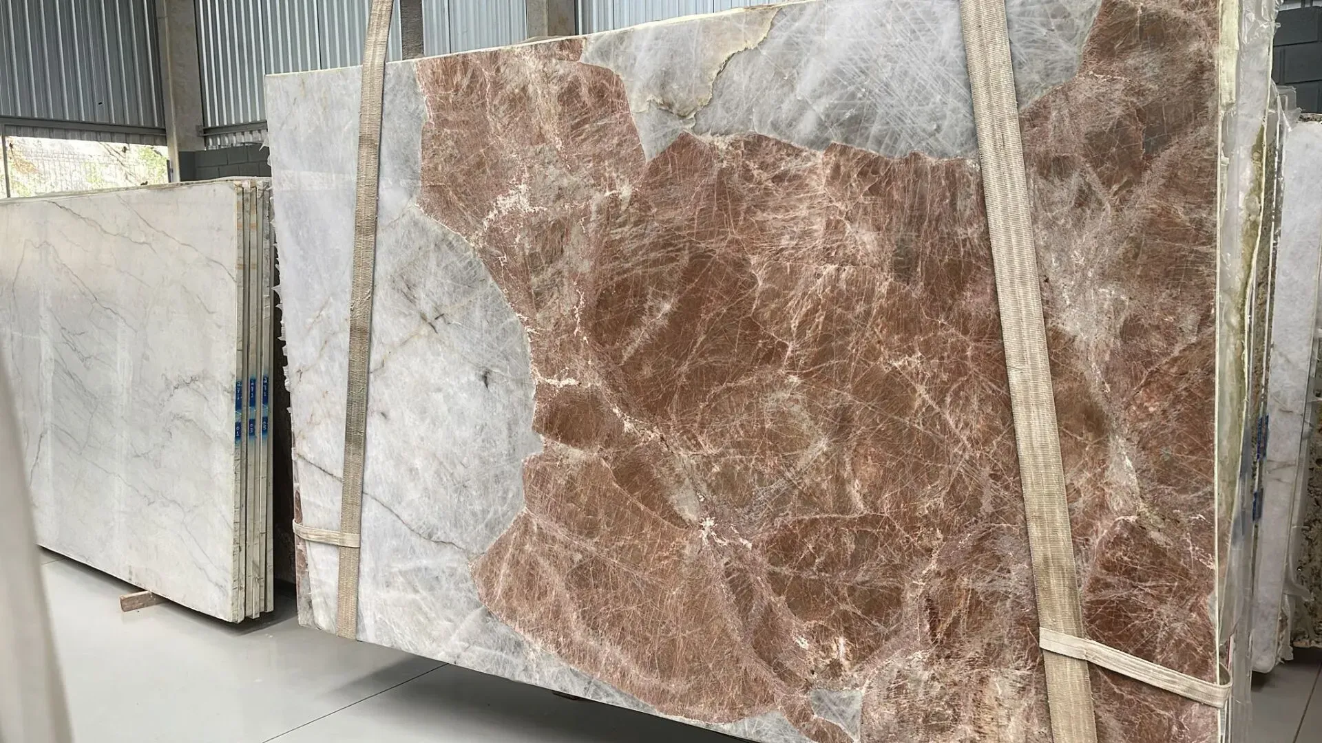 Large polished stone slabs in a warehouse, featuring white and brown veined marble patterns.