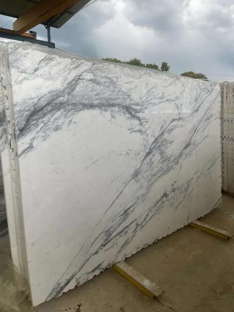 Large white marble slab with gray veining leaning on supports in an outdoor stone yard