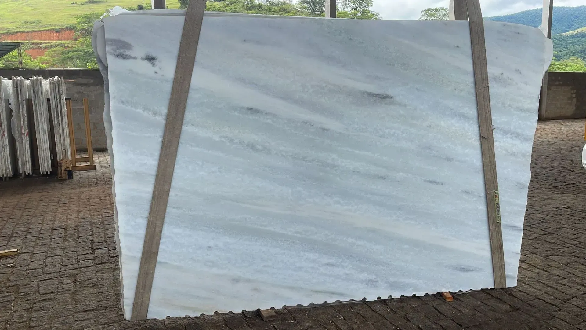 Large white slab tied upright with straps outdoors on a dirt lot