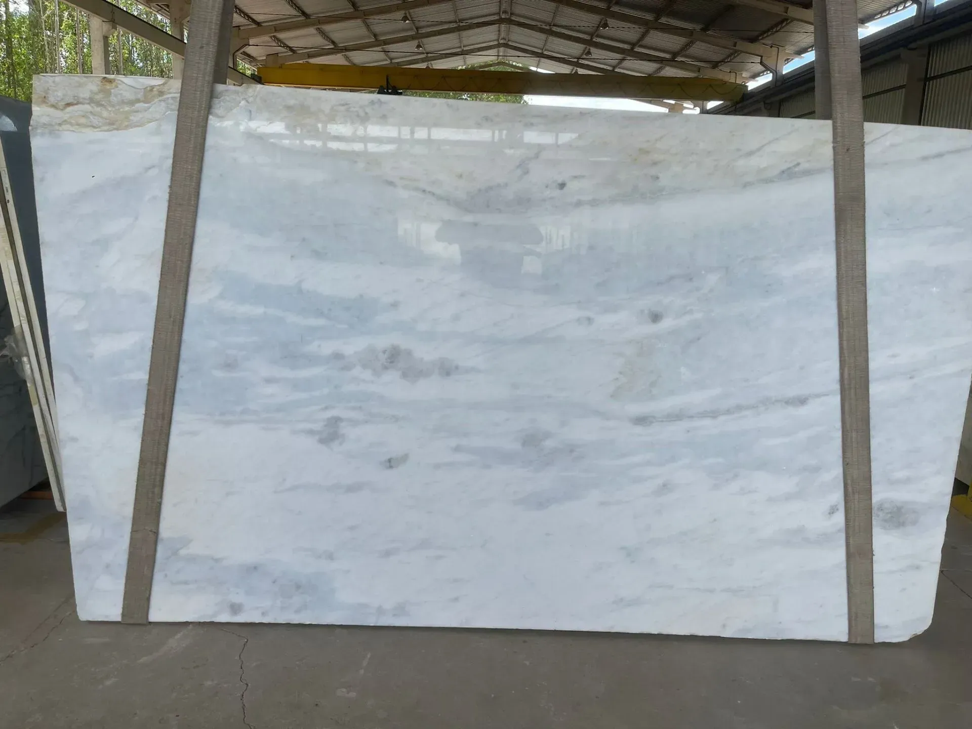 Large white marble slab displayed vertically in a warehouse, held by wooden supports.