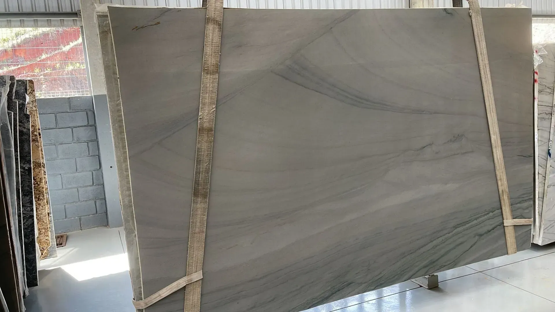 Large gray marble slab standing upright in a warehouse, supported by wooden braces.