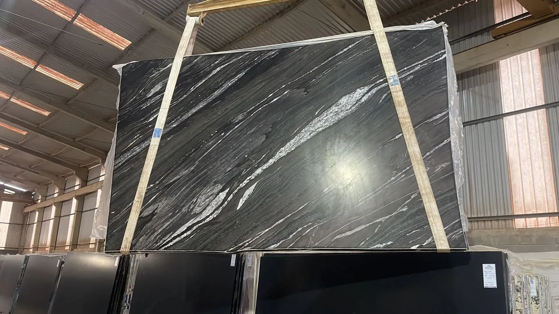 Large black marble slab wrapped in plastic, stored upright in a warehouse
