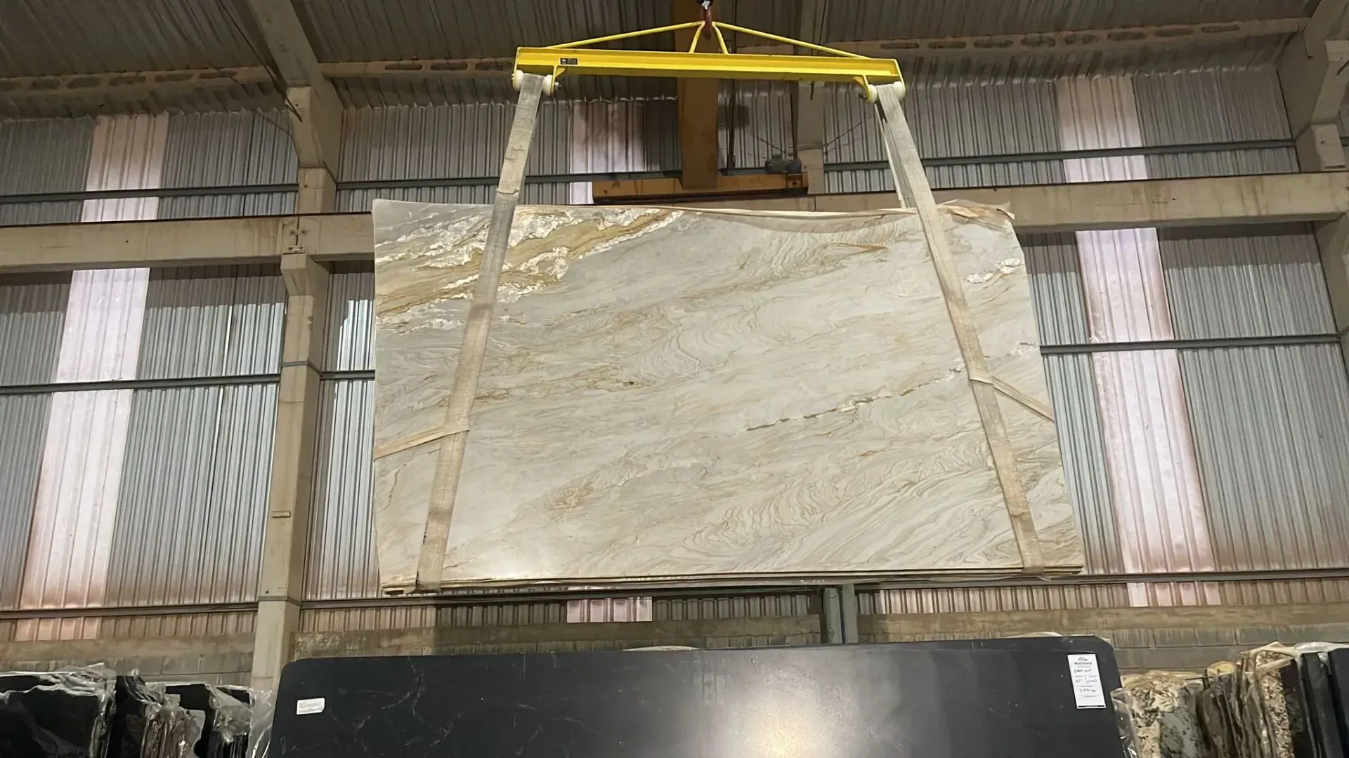 Large stone slab suspended by a yellow lifting rig inside a warehouse