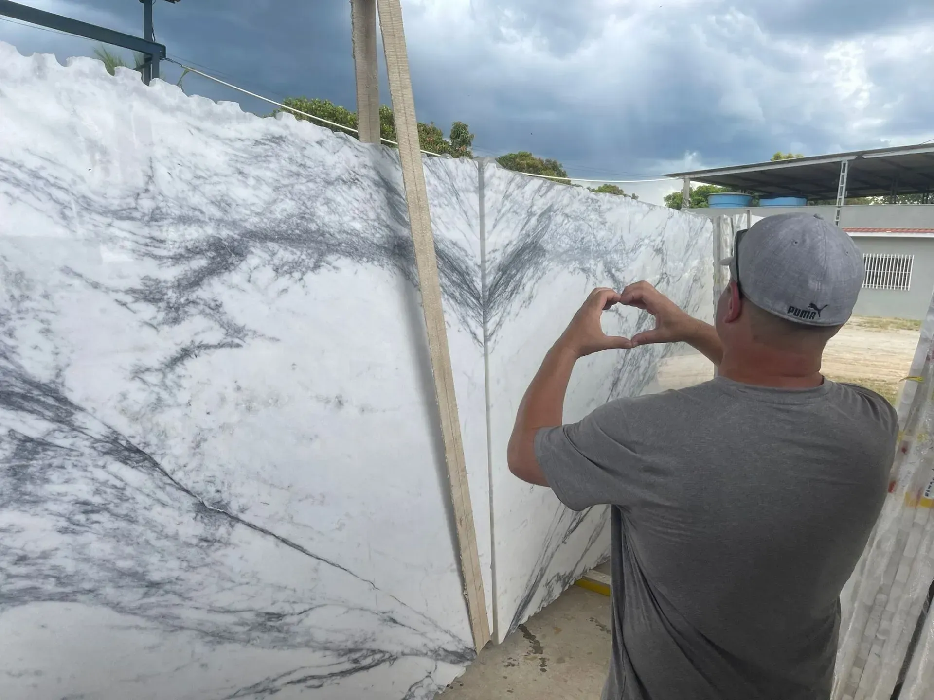 Man taking a photo of a large white marble slab outdoors under a cloudy sky