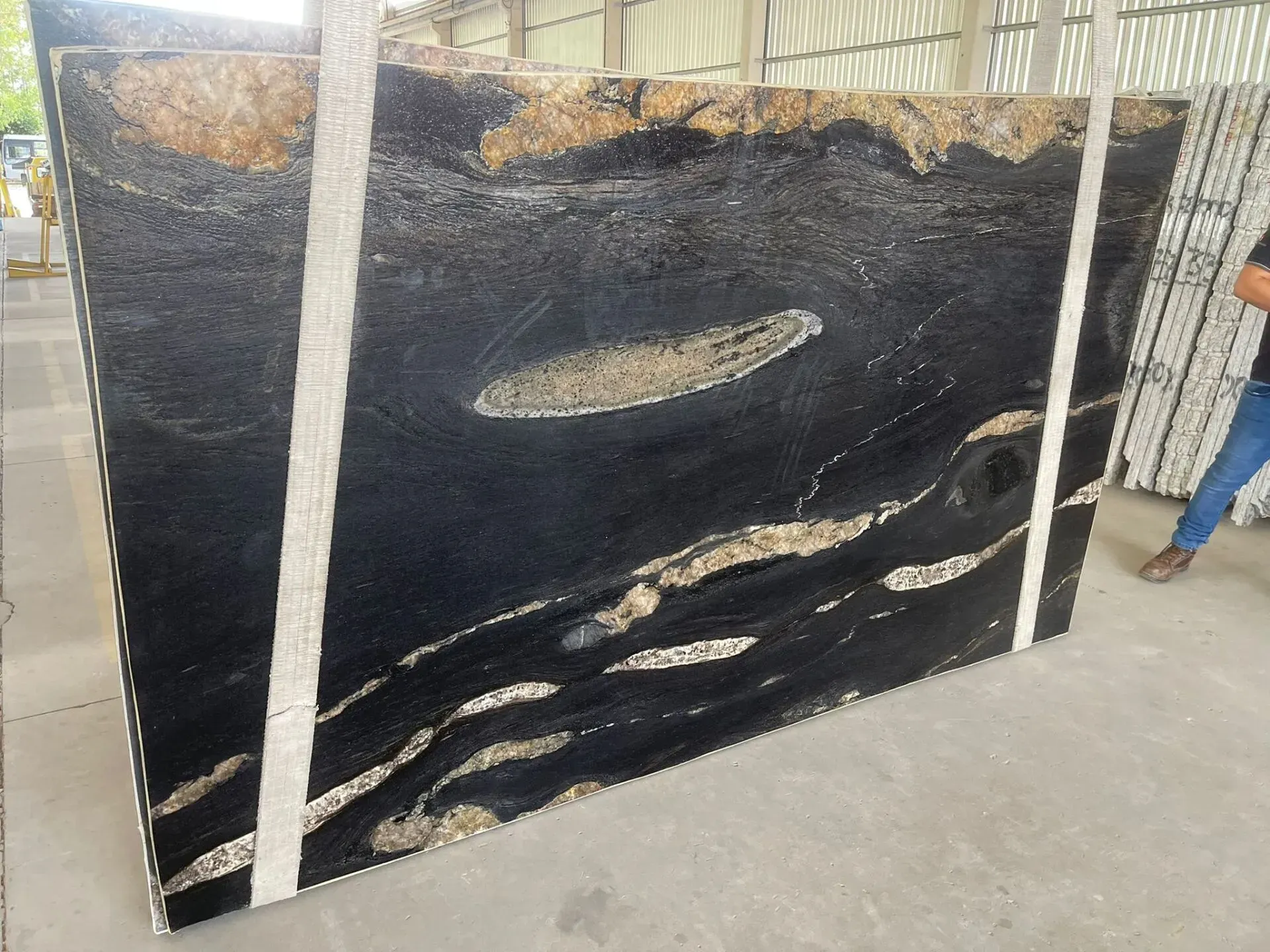 Large black marble slab with white veining, leaning upright in a warehouse or workshop.