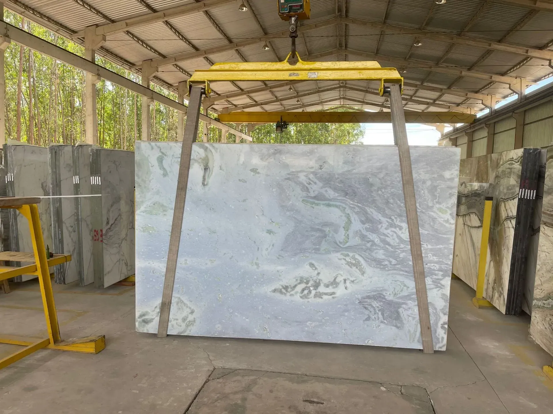 Large white stone slab hanging in a workshop under a yellow overhead crane.