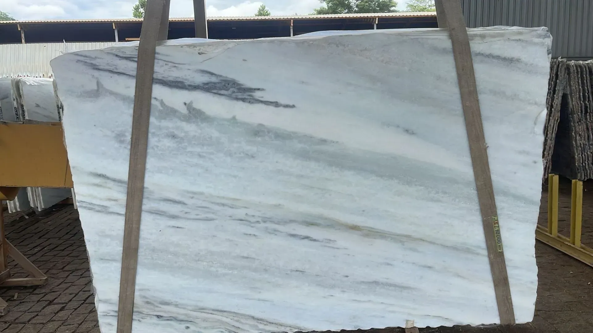 Large white marble slab with gray veining, strapped upright on a pallet outdoors