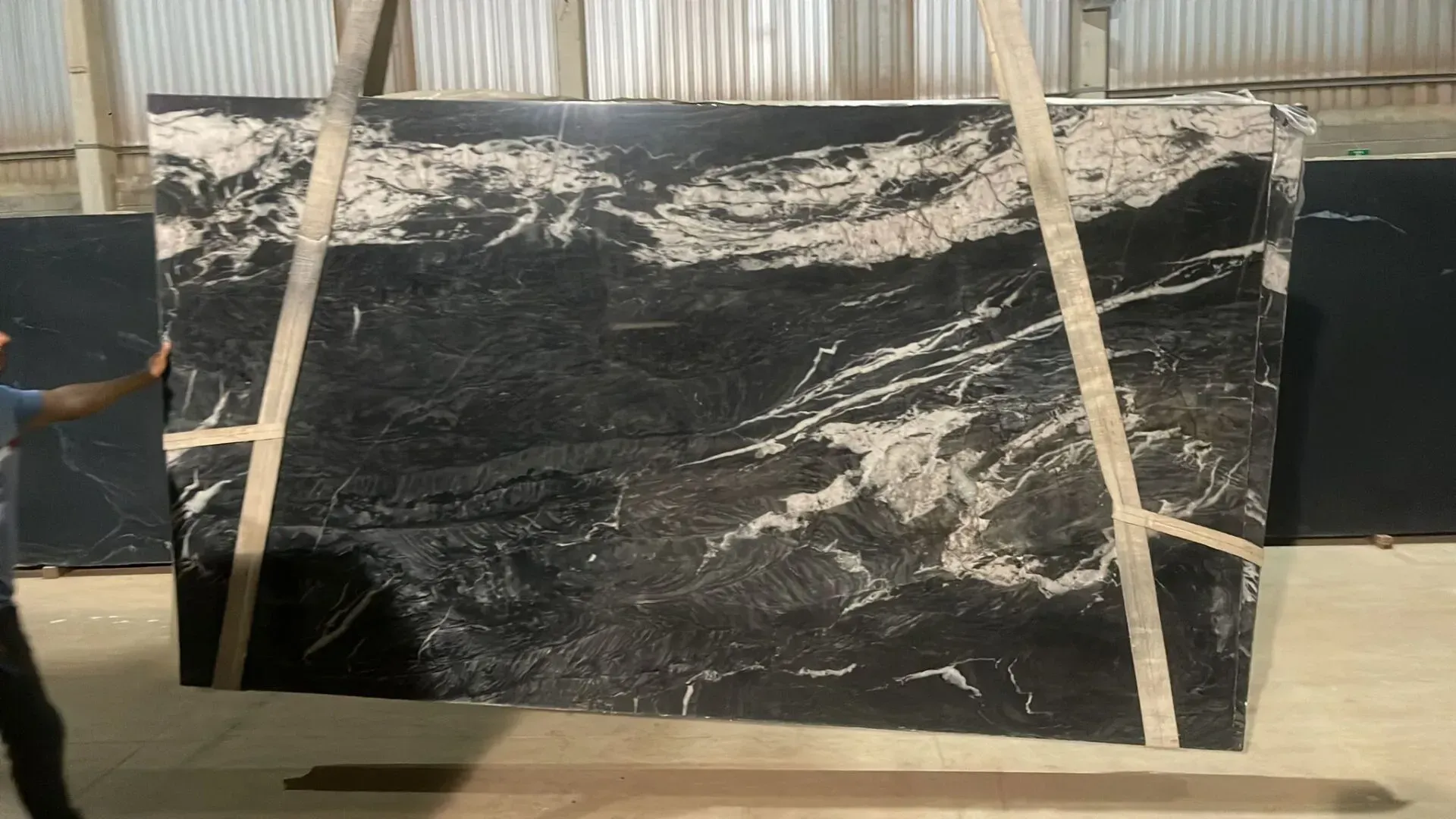 Black marble slab with white veining, strapped upright on a wooden pallet in an industrial setting