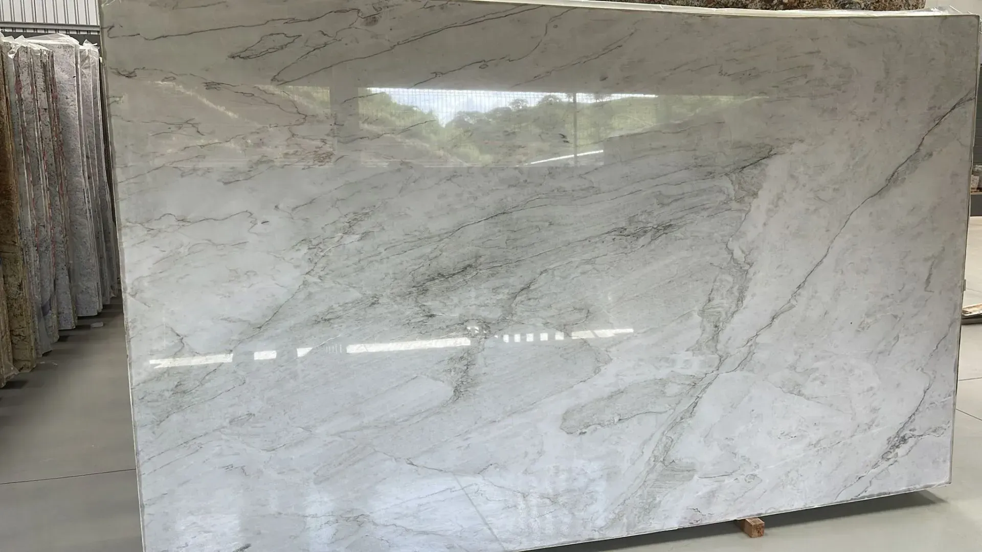 Large white marble slab with gray veining displayed upright in a warehouse or stone yard