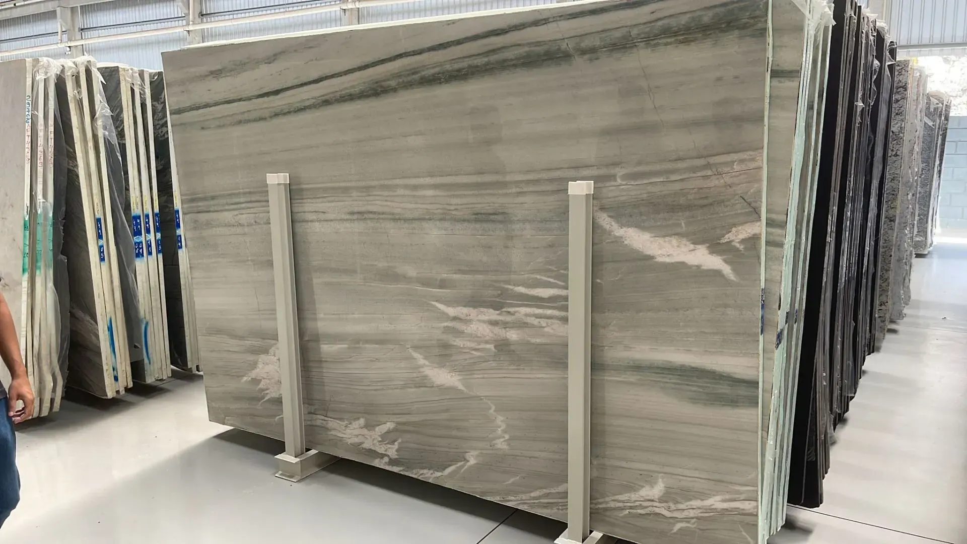 Stacks of large beige stone slabs wrapped in plastic in a warehouse showroom aisle