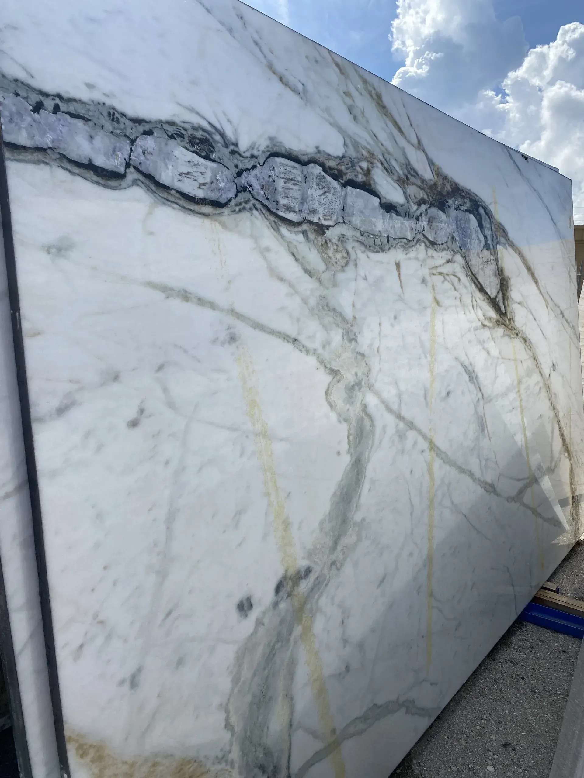 Large white marble slab with gray veining leaning outdoors against a sky background