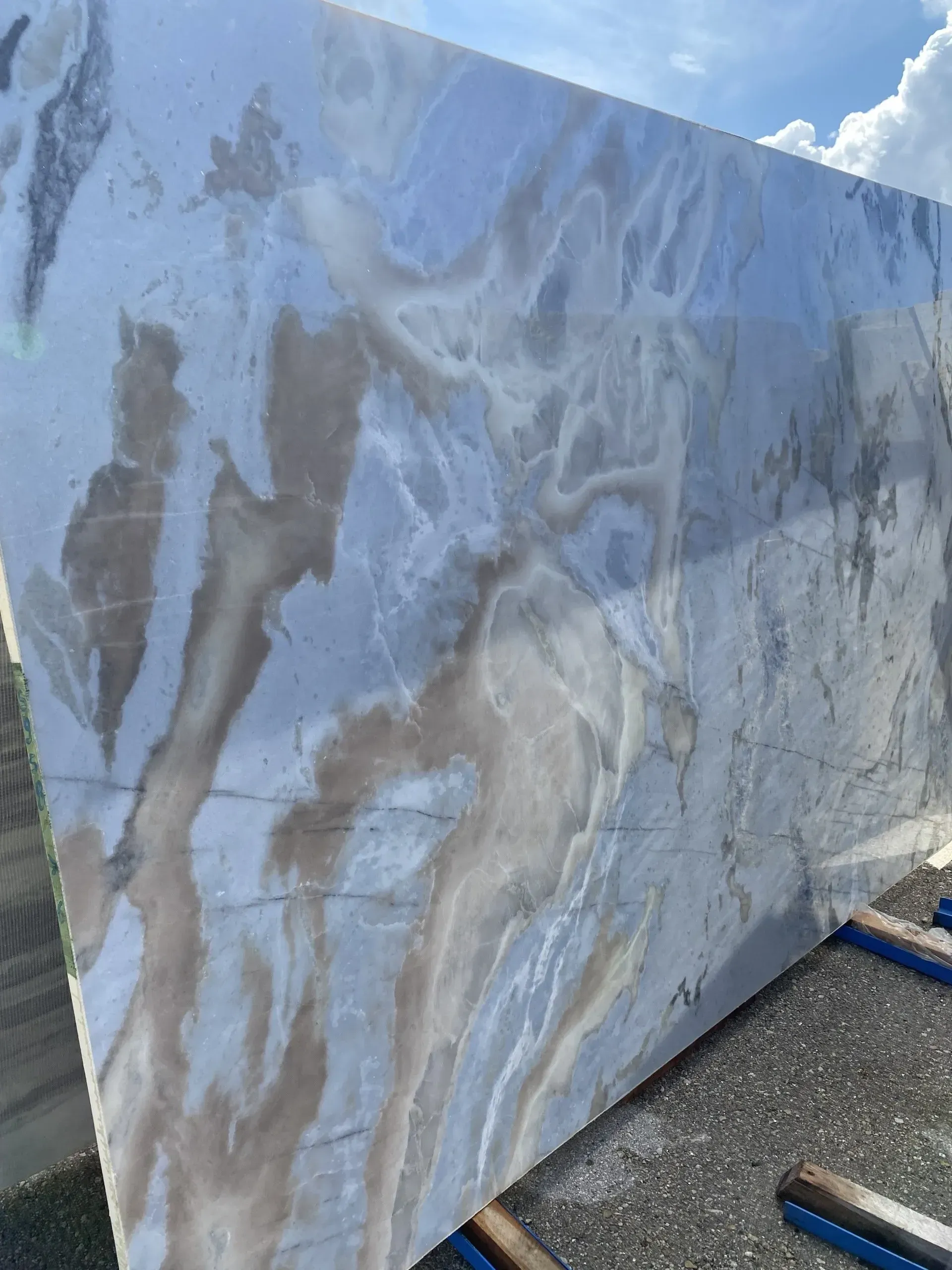 Marble slab with gray-blue veining leaning outdoors on gravel near pipes