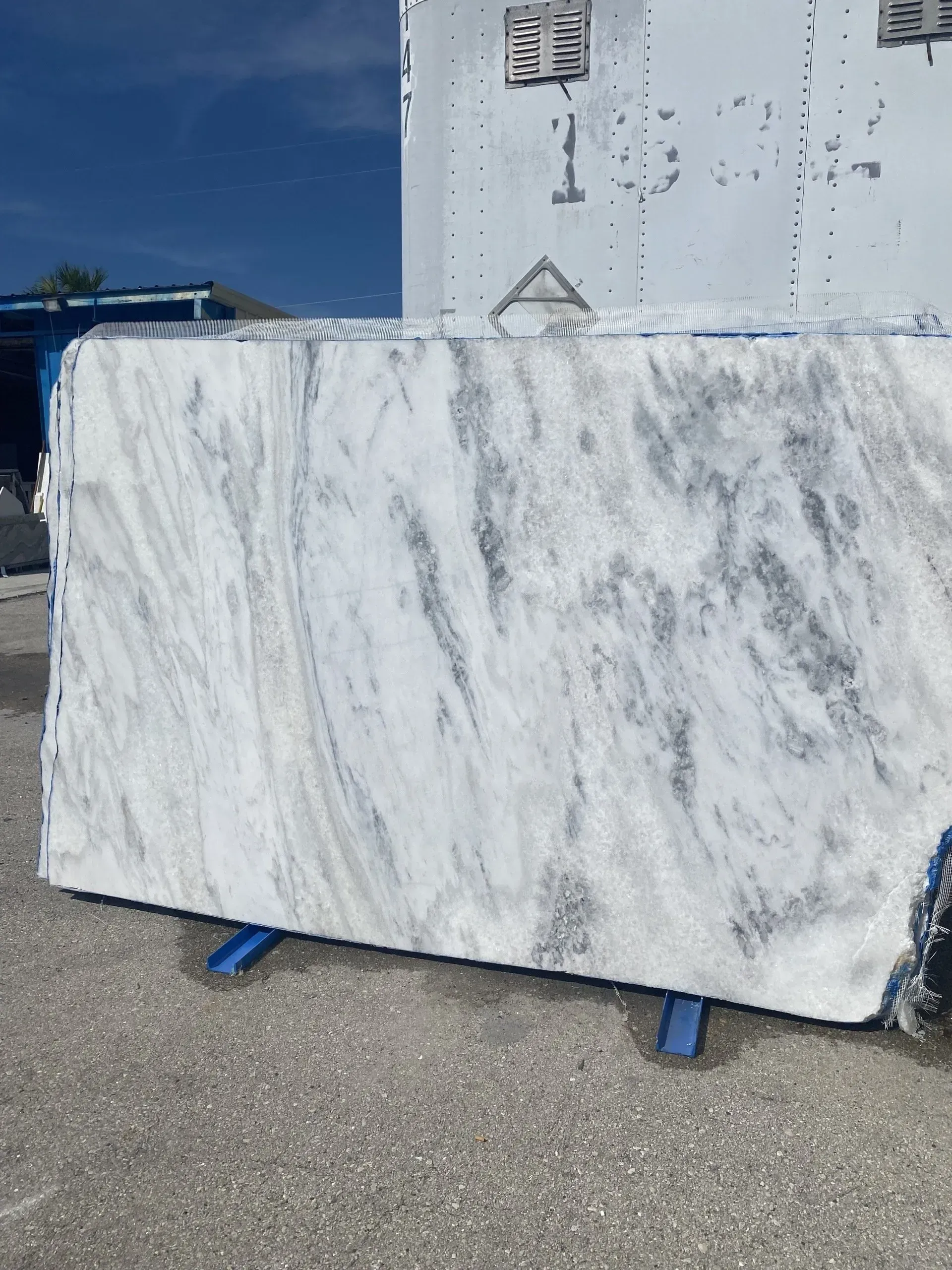 Large white marble slab on blue supports outdoors beside a white truck trailer