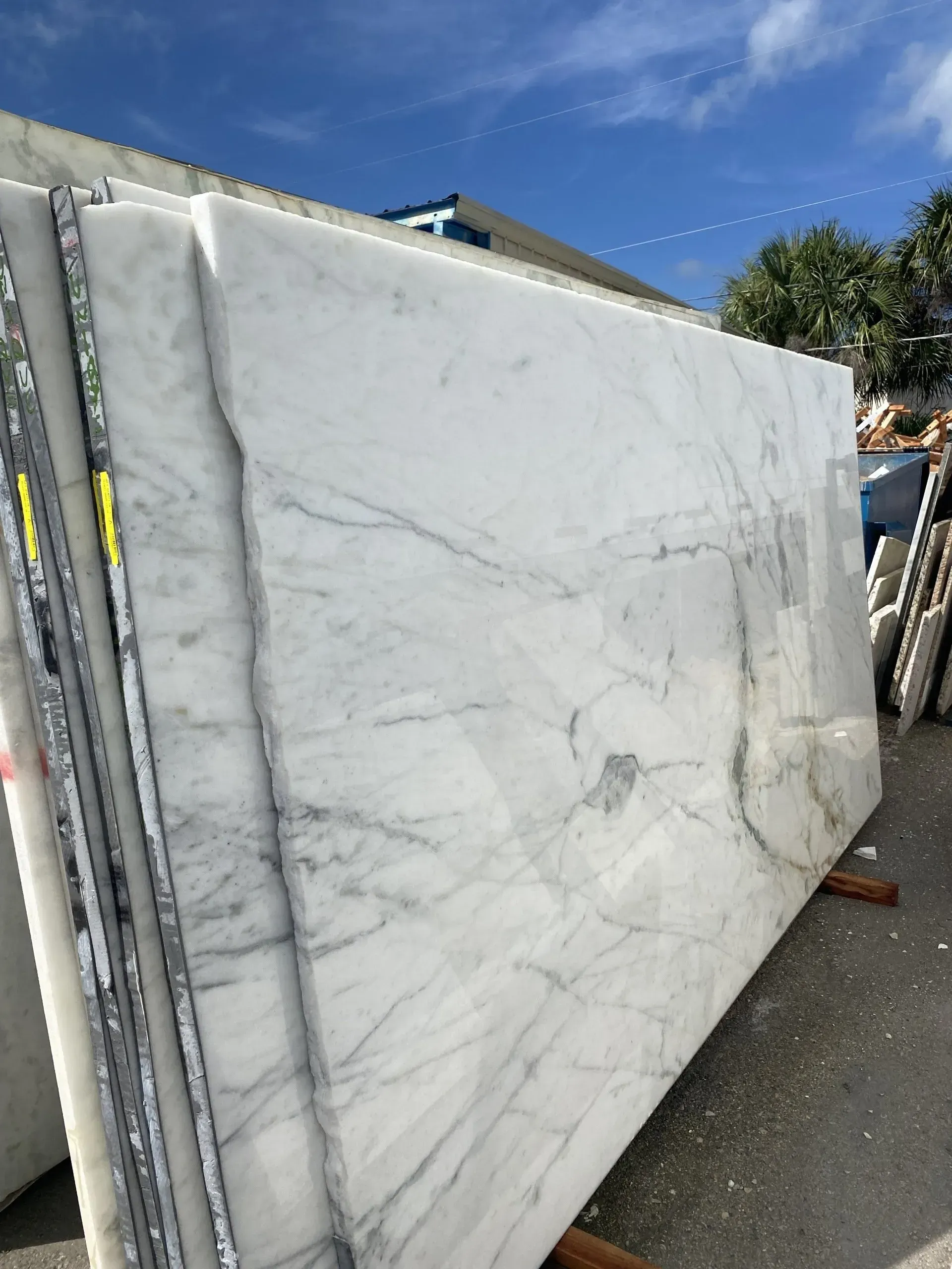 Large white marble slabs stacked outdoors in a stone yard, with gray veining visible.