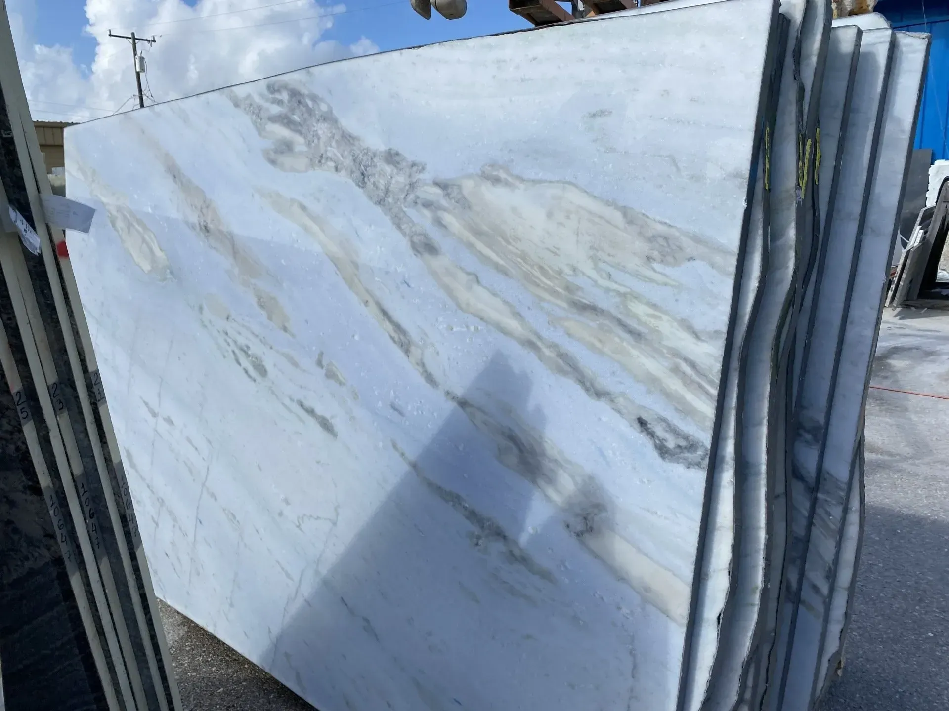 Stacked white marble slabs with gray veining displayed outdoors on a metal rack