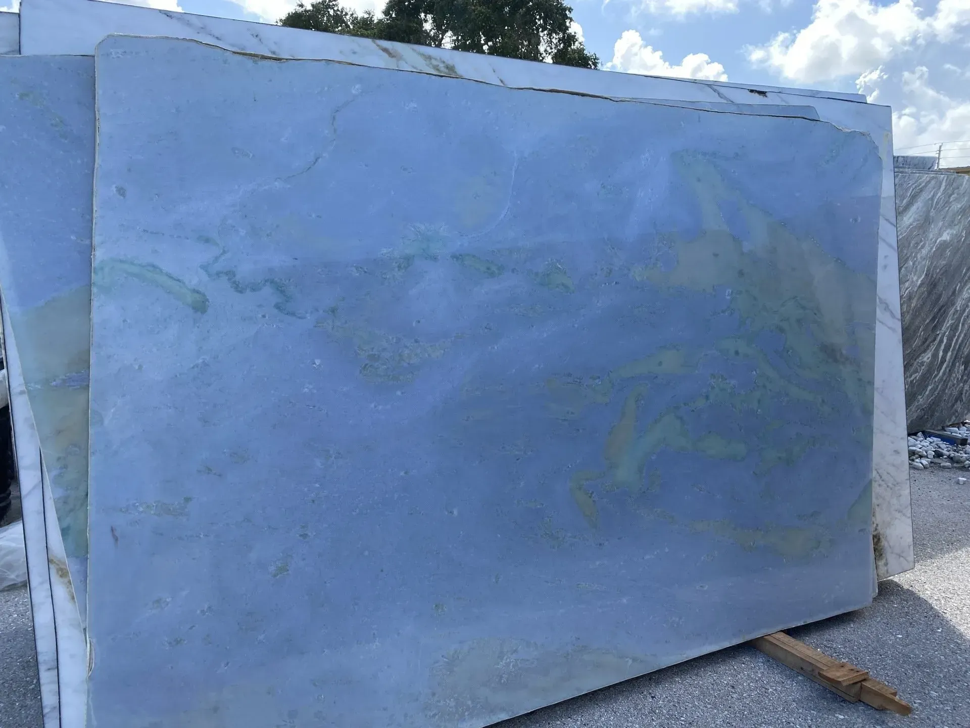 Large blue-tinted glass or acrylic panel leaning outdoors against a wall.