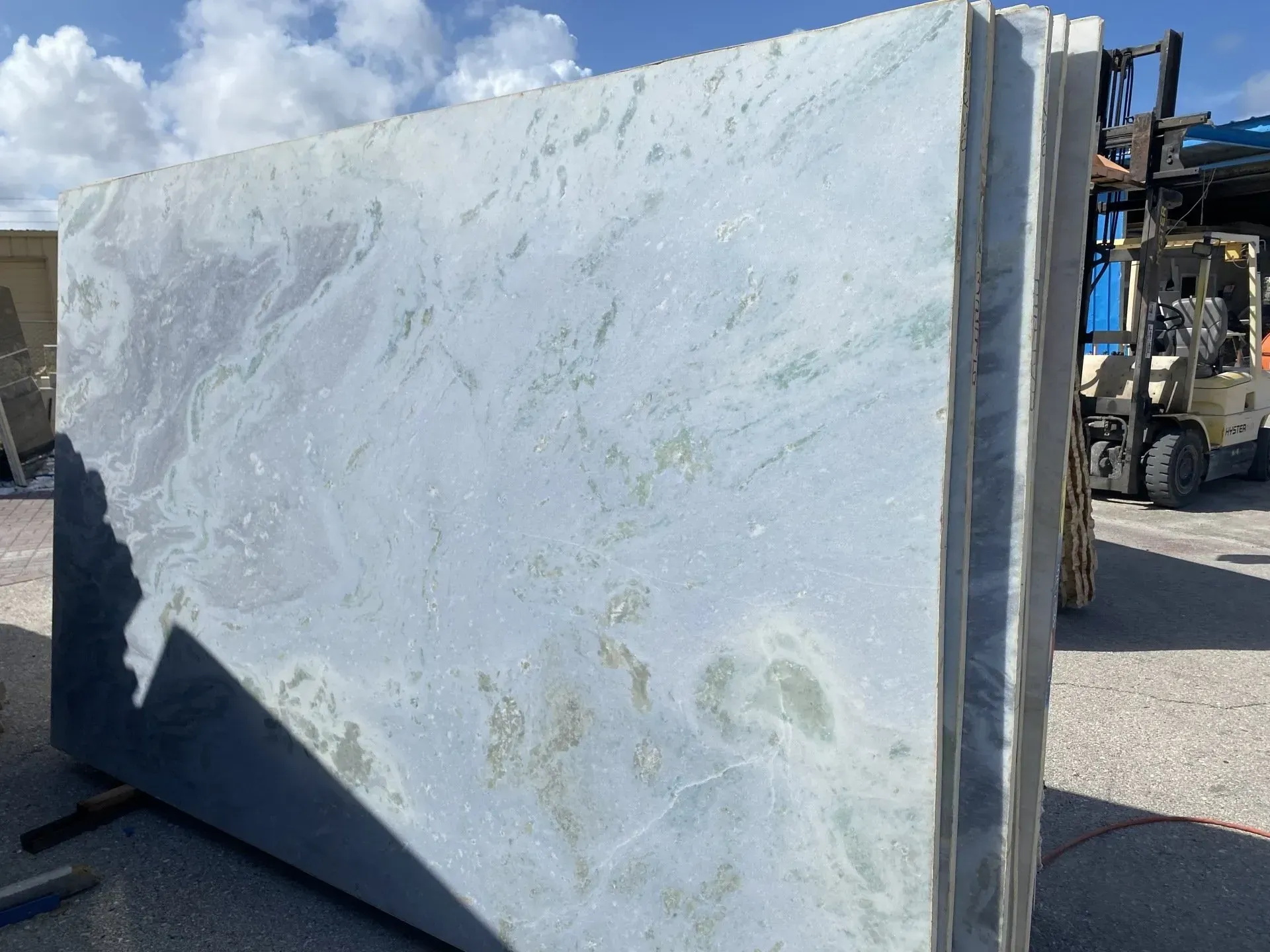 Large white marble slabs leaning upright in an outdoor industrial yard, with a forklift nearby.