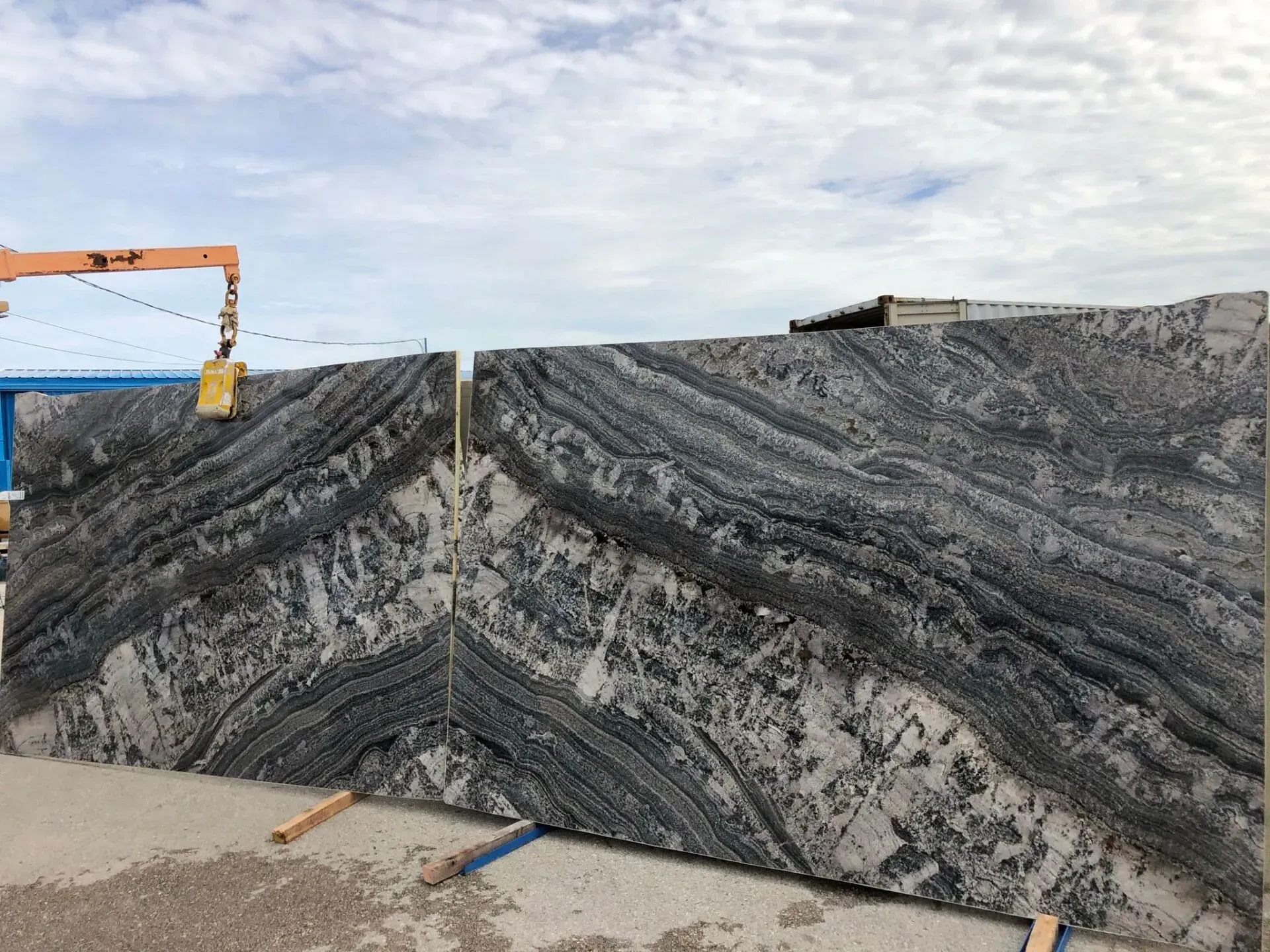 Large striped stone slabs at an outdoor yard, with an orange crane arm on the left.
