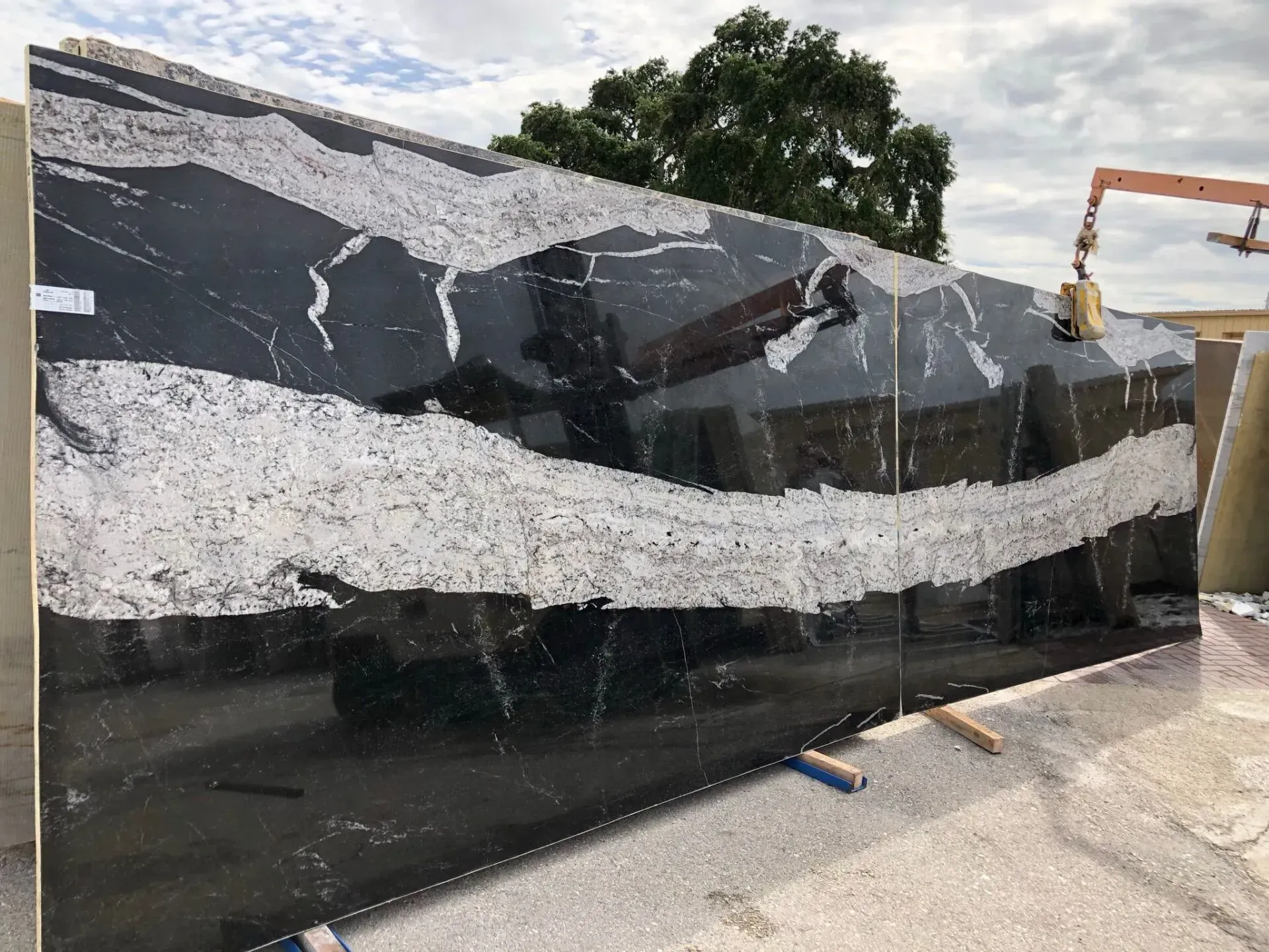 Large polished black-and-white stone slab being moved outdoors by a crane in a yard.