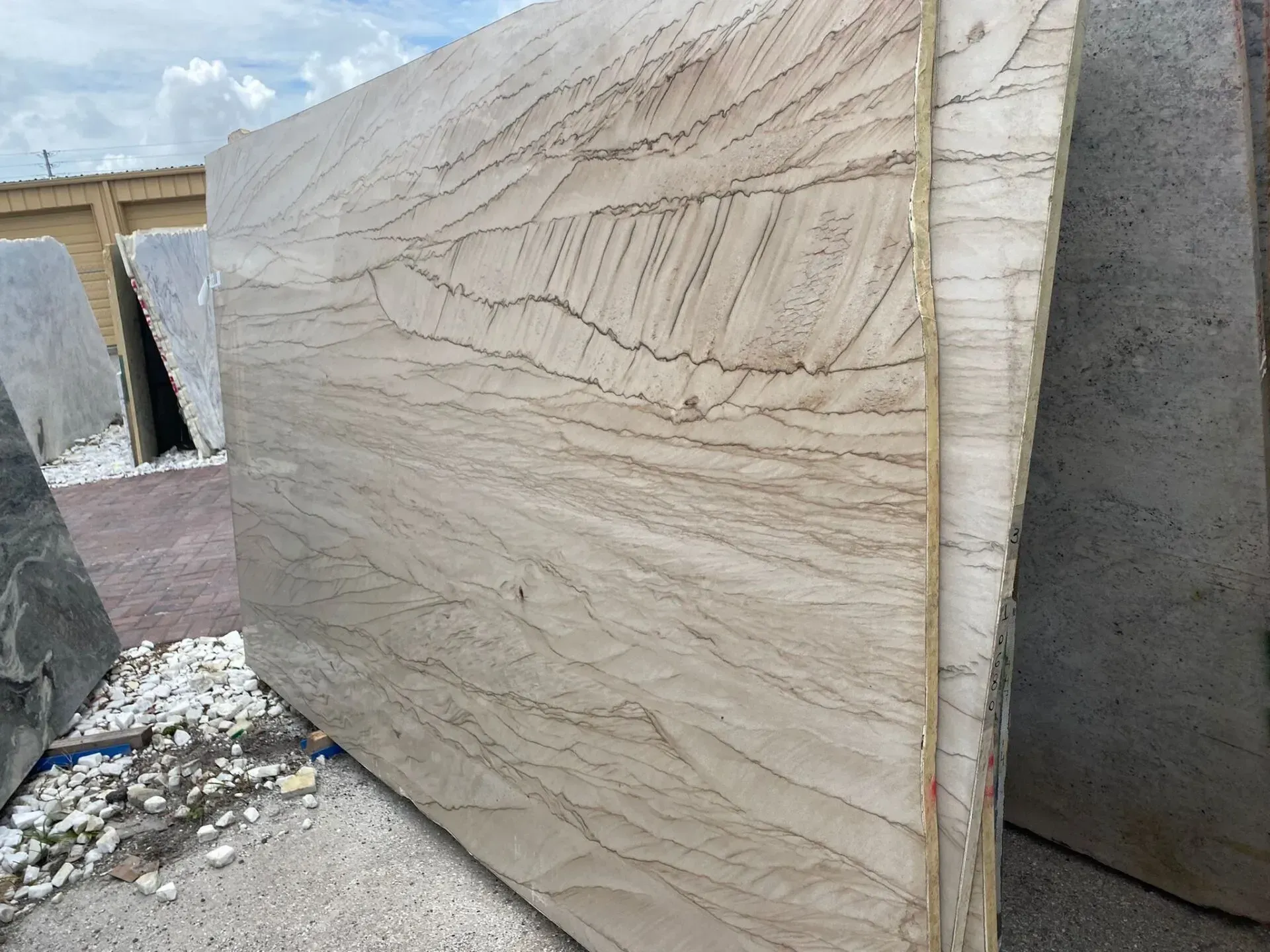 Large beige stone slabs stacked outdoors in a stone yard, with visible veining and rough edges