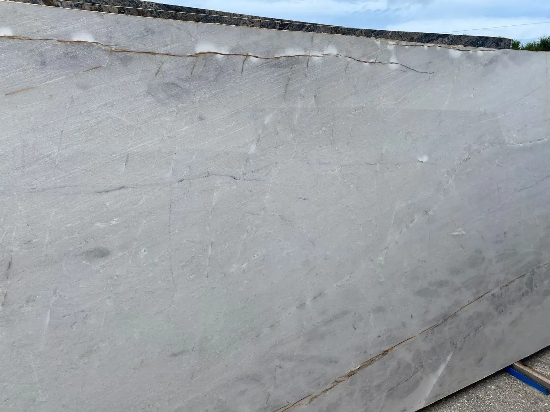 Close-up of a gray concrete wall with cracks and weathered texture beneath a cloudy sky.