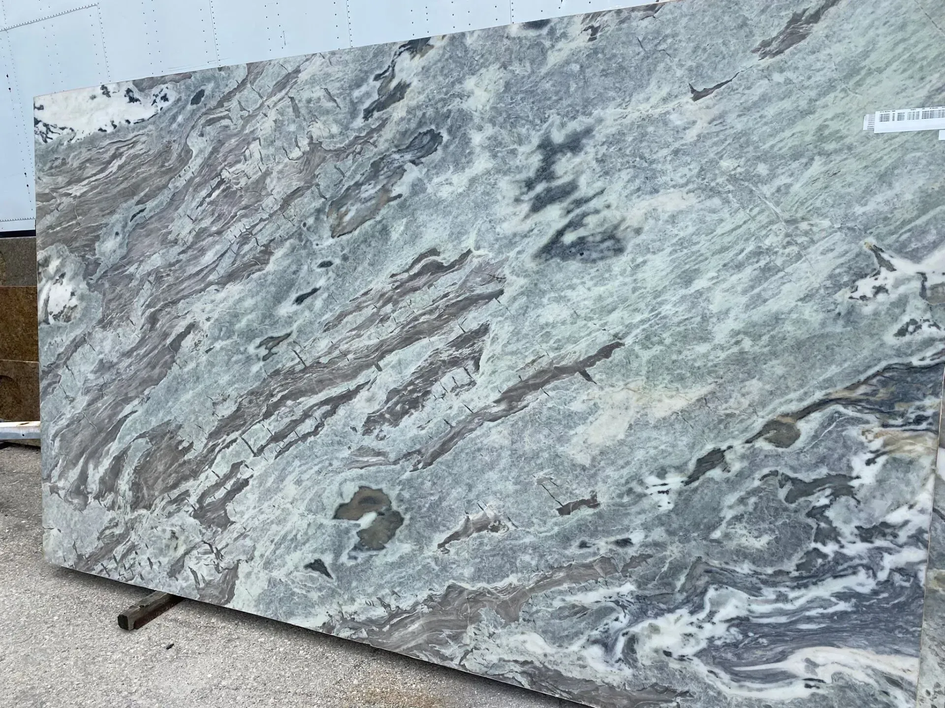 Large slab of gray and white veined stone leaning outdoors on wooden supports