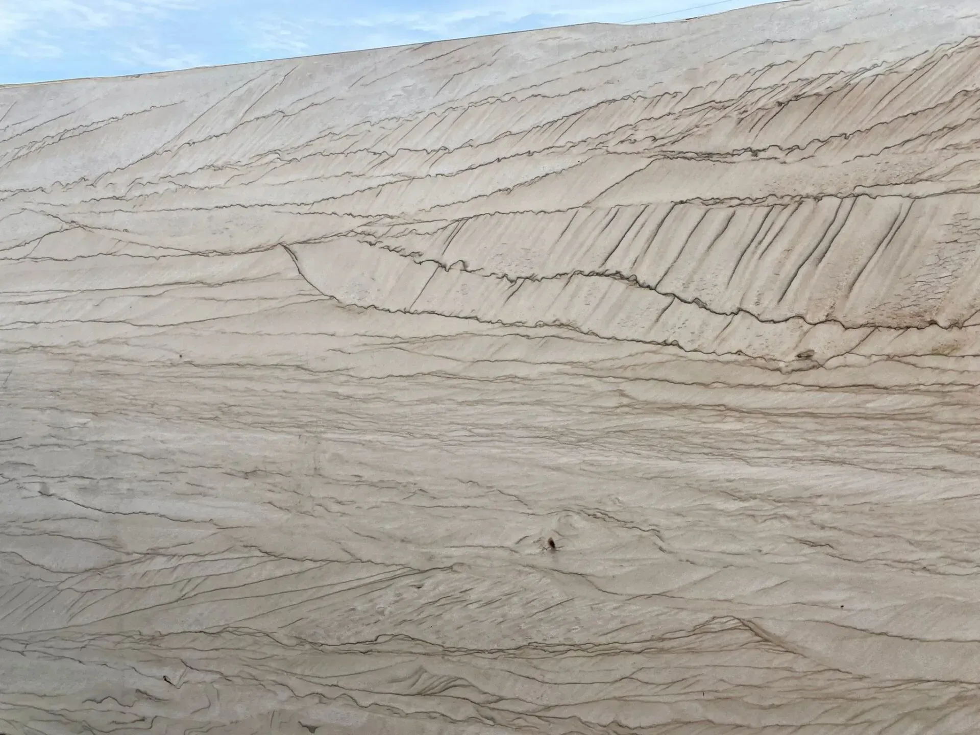 Light beige sand dune with rippled layers under a pale blue sky