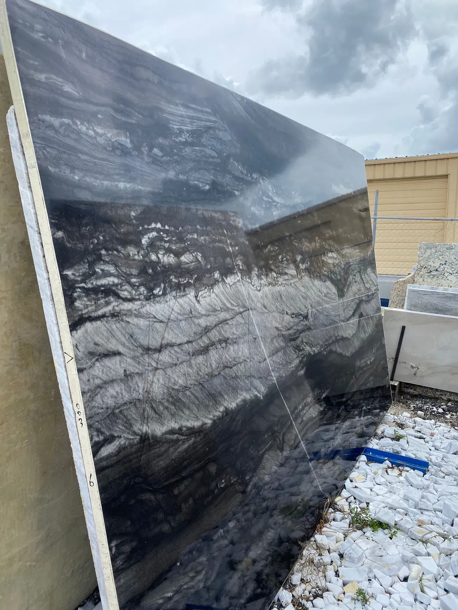 Large dark abstract panel leaning outdoors beside a snowy ground and beige building