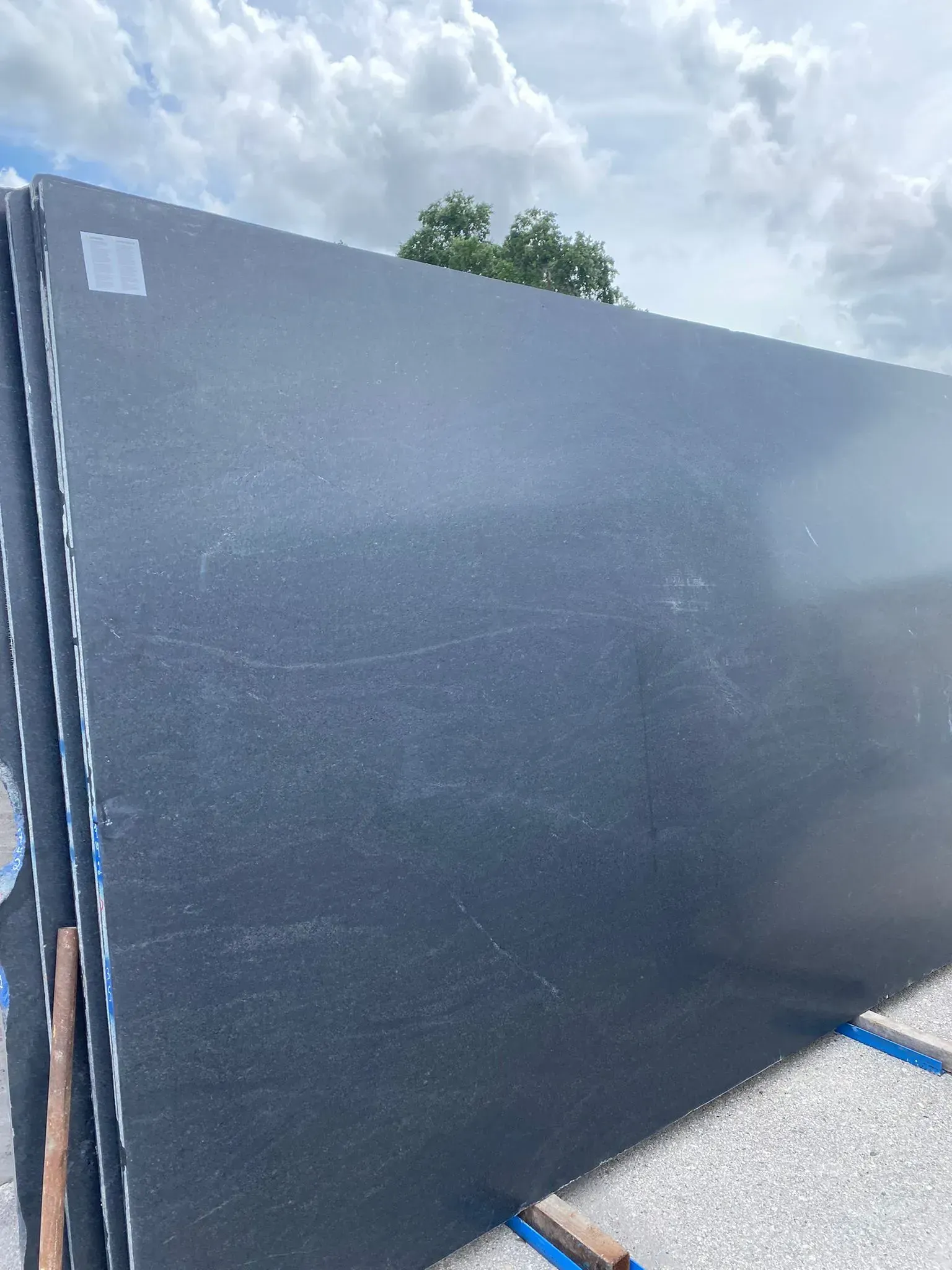 Large black foam board leaning outdoors on gravel under a cloudy sky