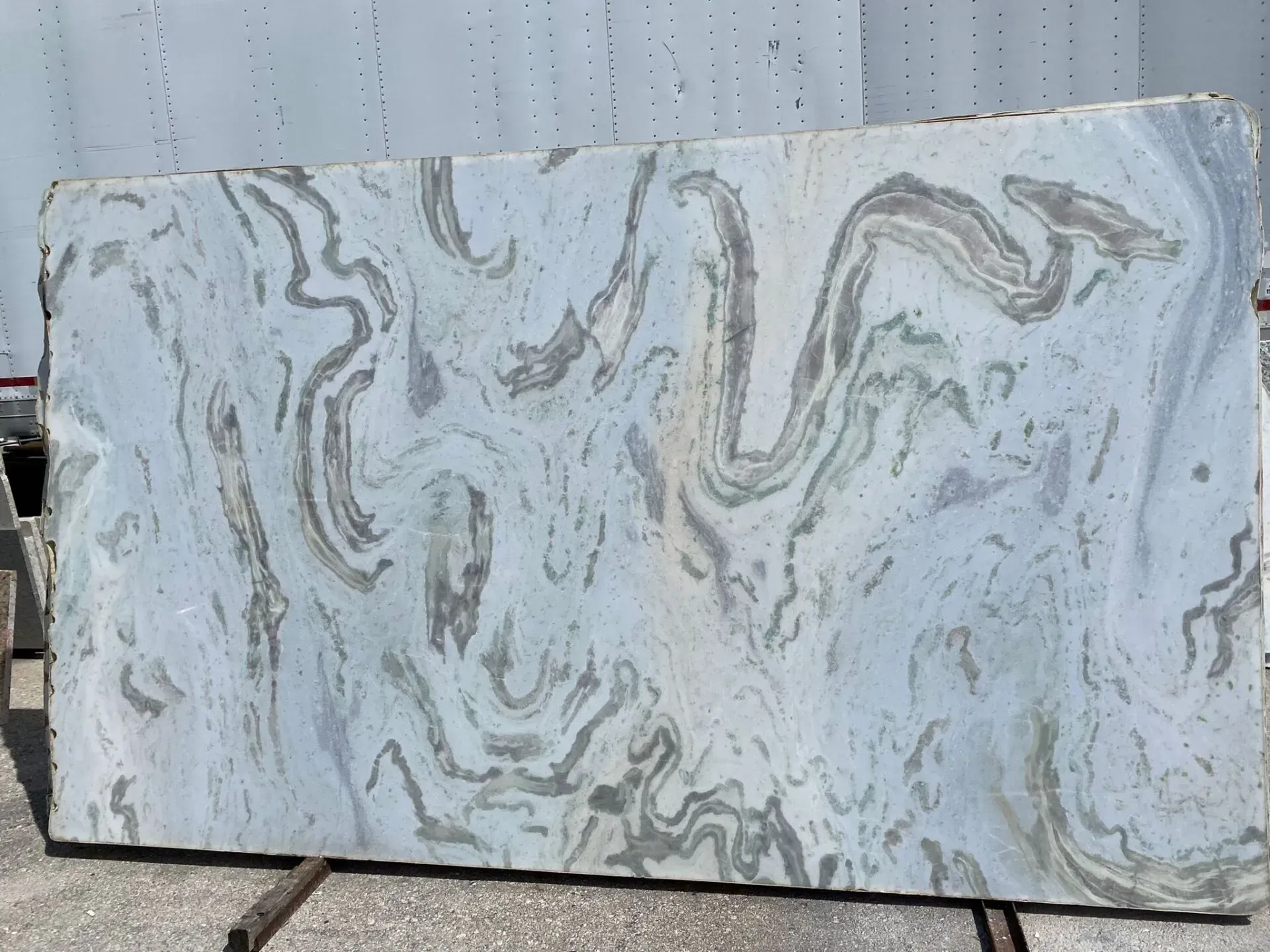 Rectangular white slab with gray and tan marble-like swirls, leaning against a wall outdoors