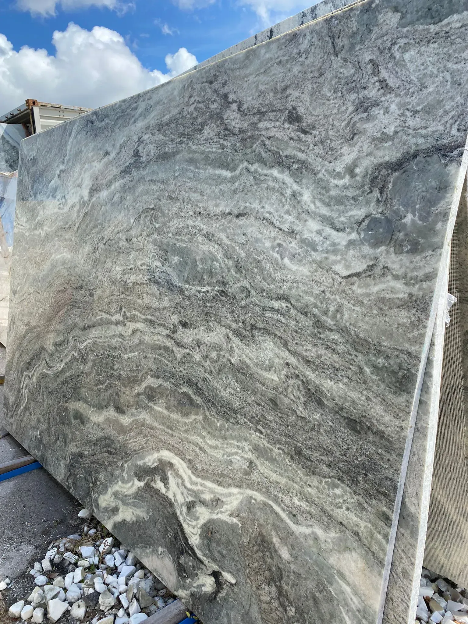 Large gray-and-white granite slab standing outdoors beside gravel and a blue hose