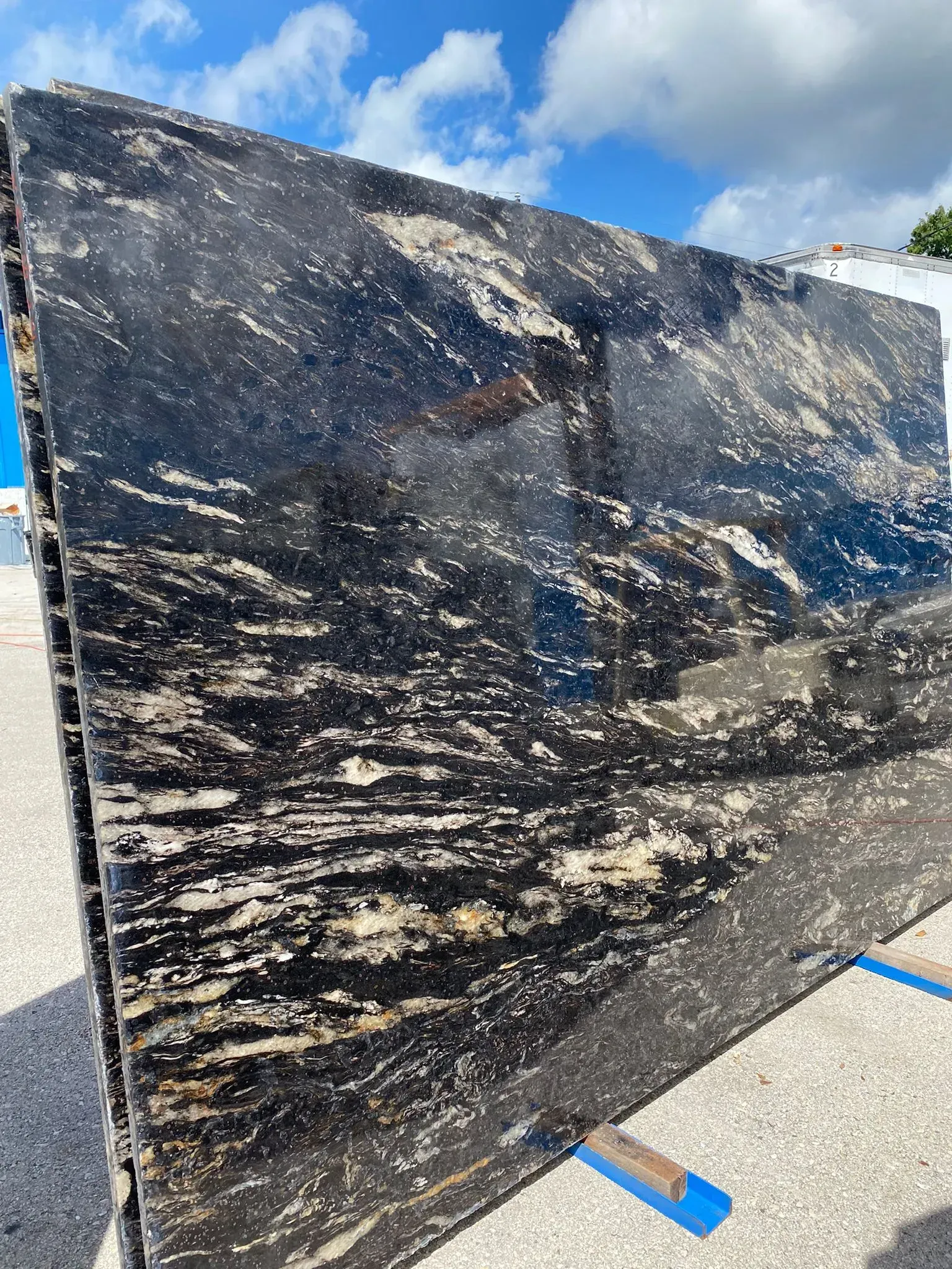 Large black marble slab with white veining displayed outdoors on blue supports