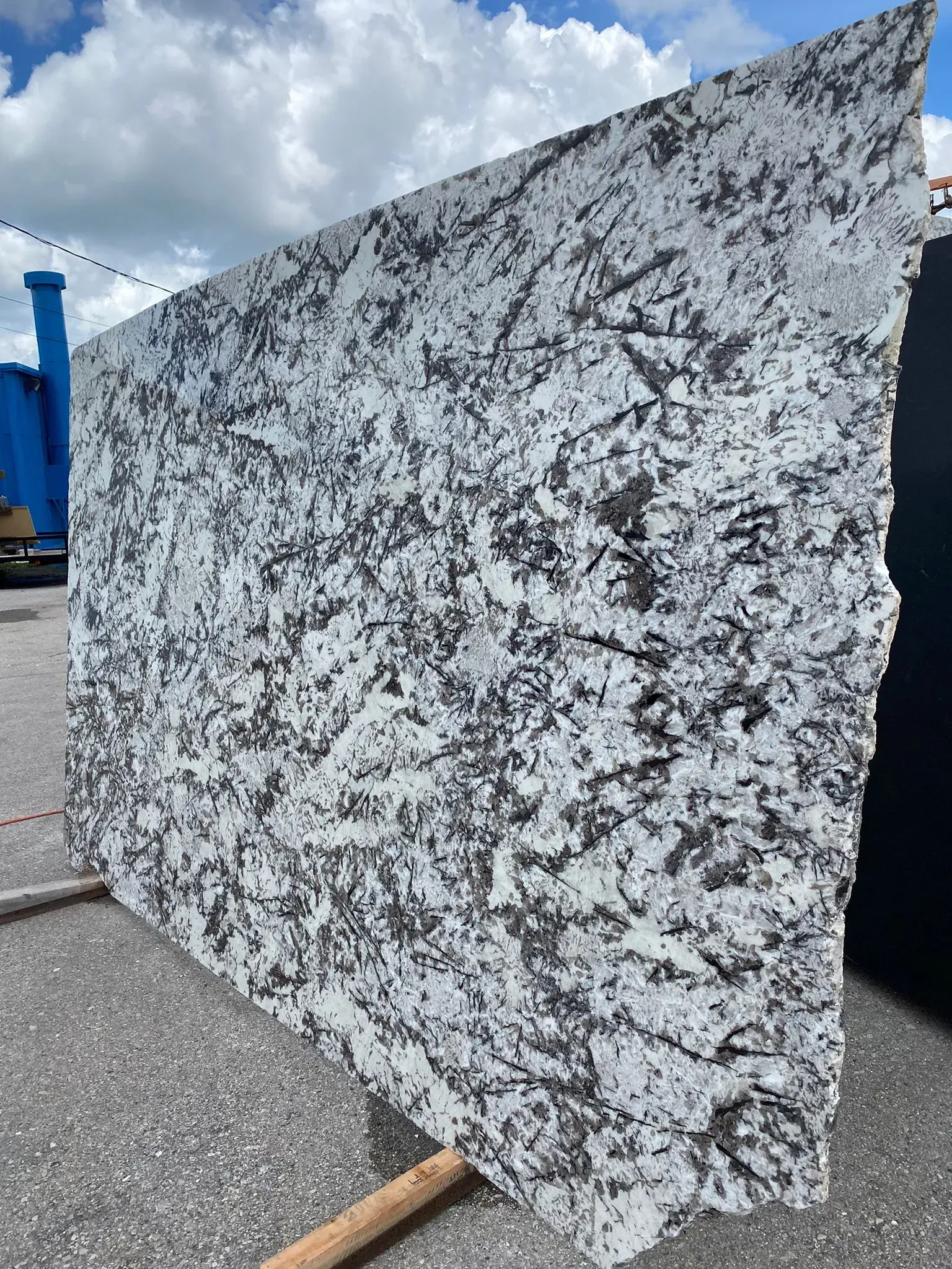 Large speckled granite slab standing outdoors on wooden supports under a cloudy sky