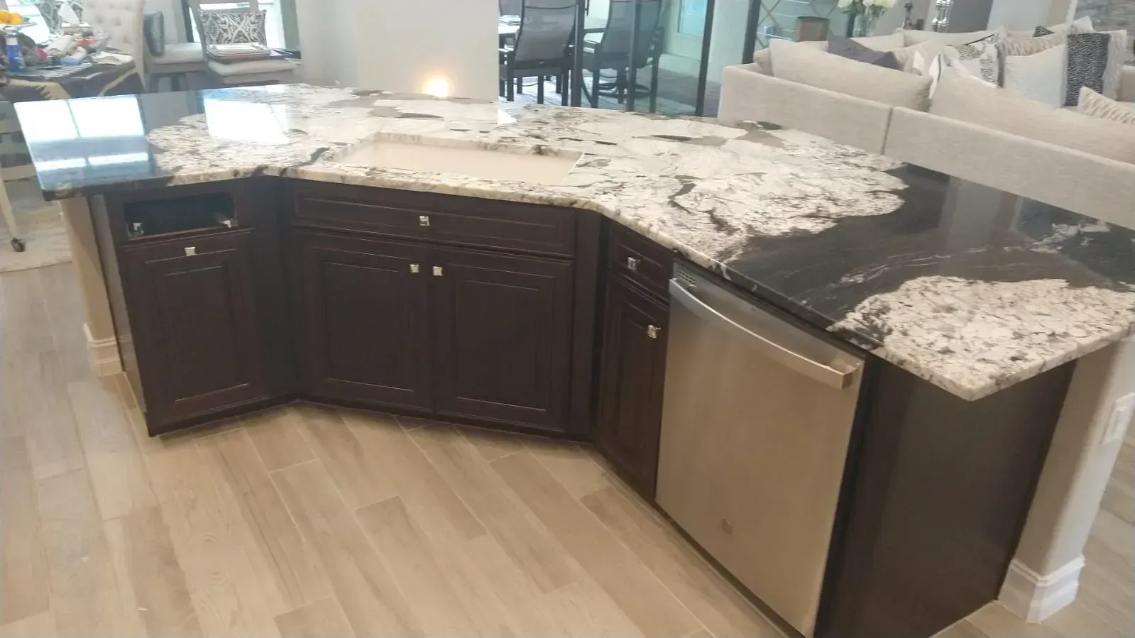 Curved kitchen island with granite countertop, dark cabinets, and stainless steel dishwasher in a modern kitchen.