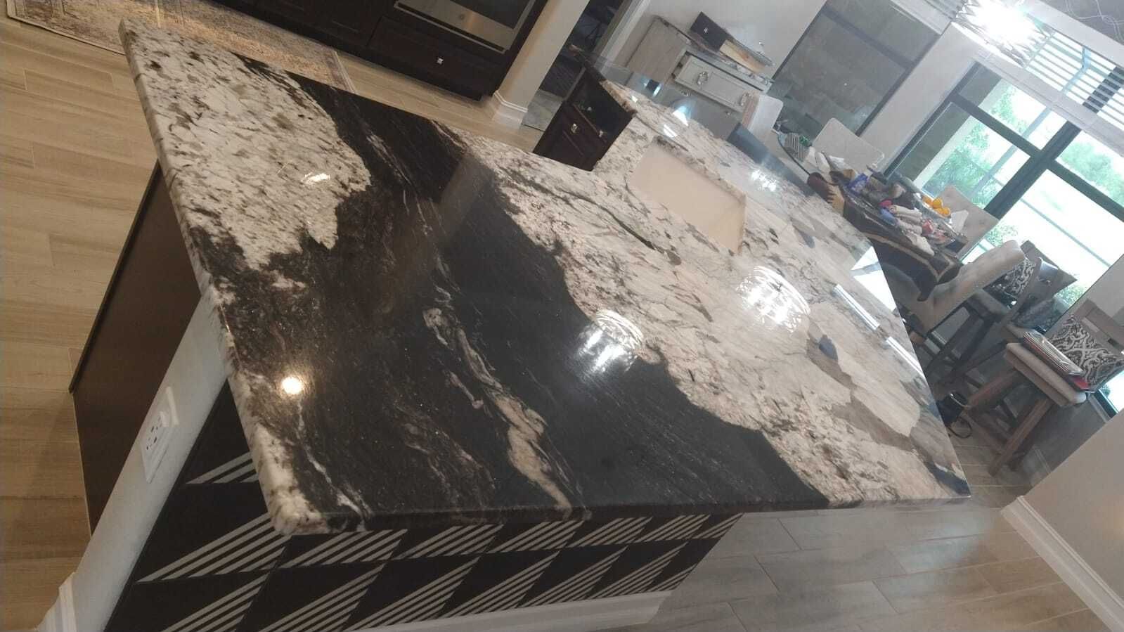 Large black-and-white marble kitchen island with waterfall edge in a modern open room.