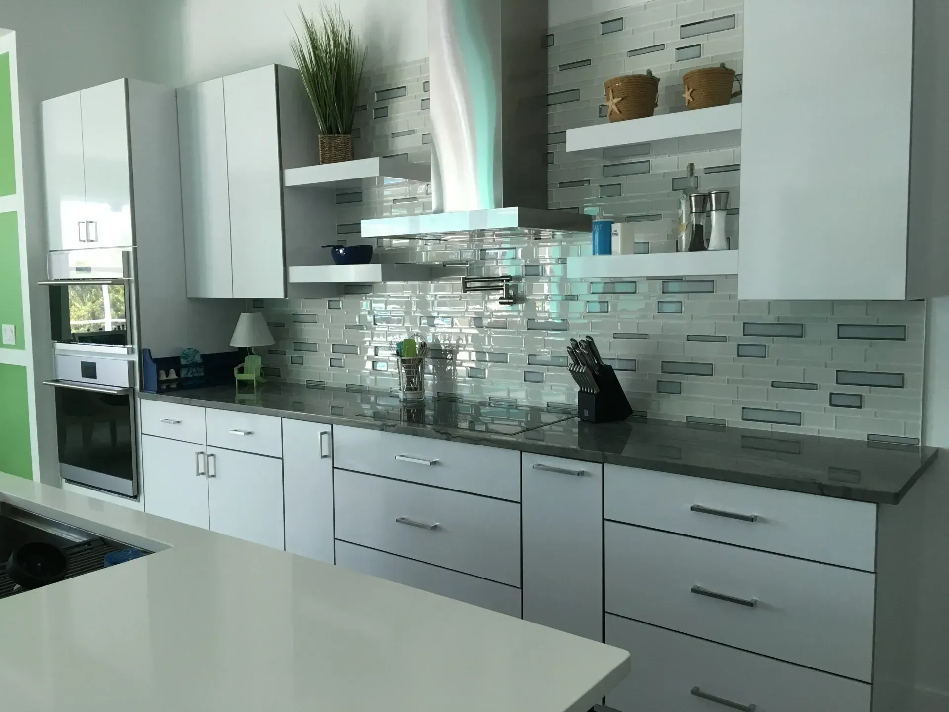 Modern white kitchen with gray countertops, glass backsplash, stainless range hood, and an island in the foreground